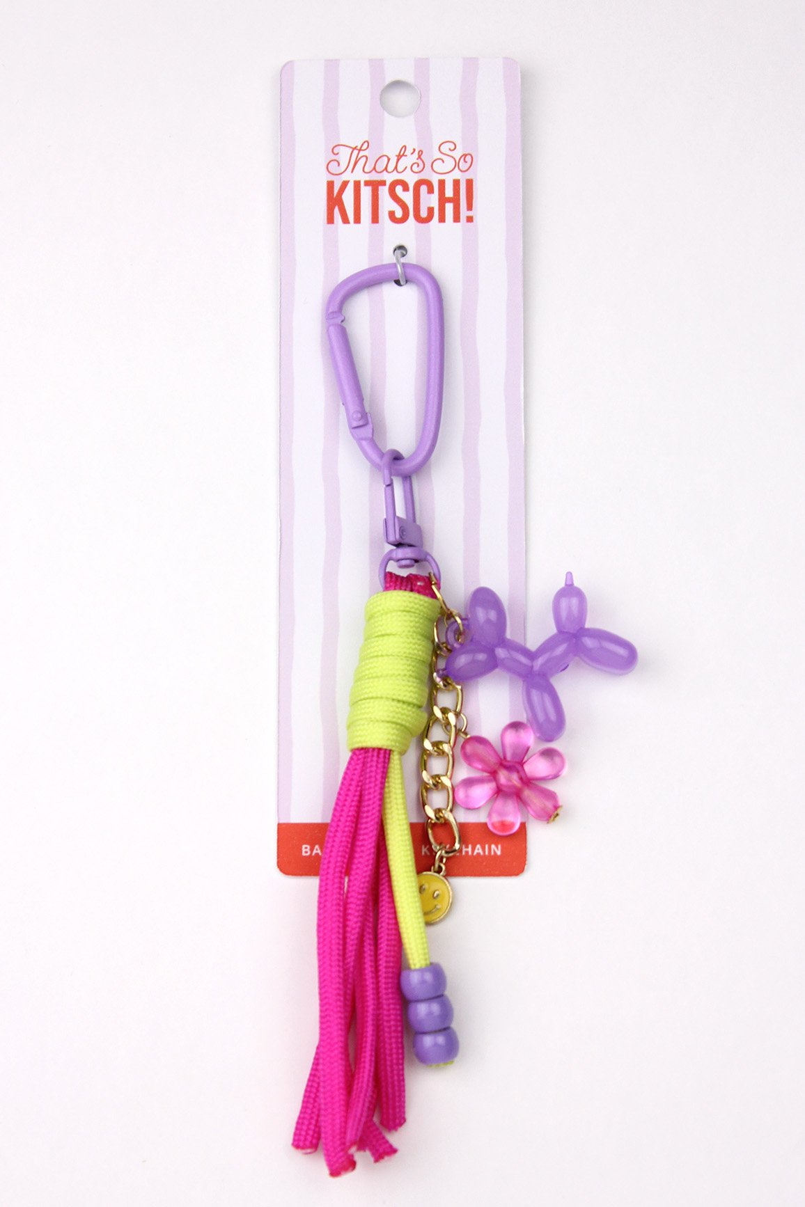 Colorful keychain with charms including a purple balloon animal, a pink flower, pink and yellow tassels, and a smiley face charm, attached to a purple clip on packaging that reads 'That's So KITSCH!'