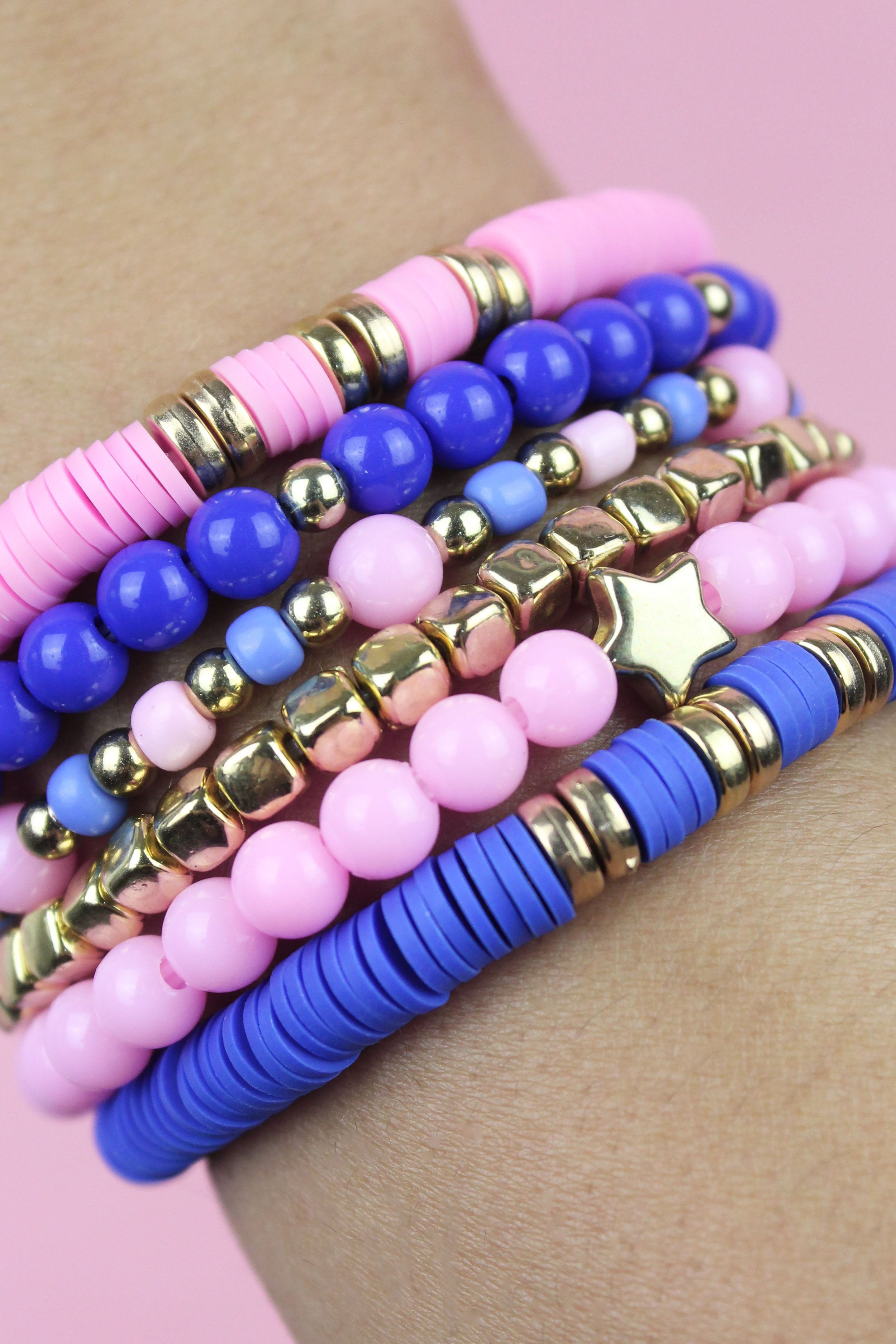 Colorful beaded bracelets in pink, blue, purple, and gold worn on a wrist against a pink background.