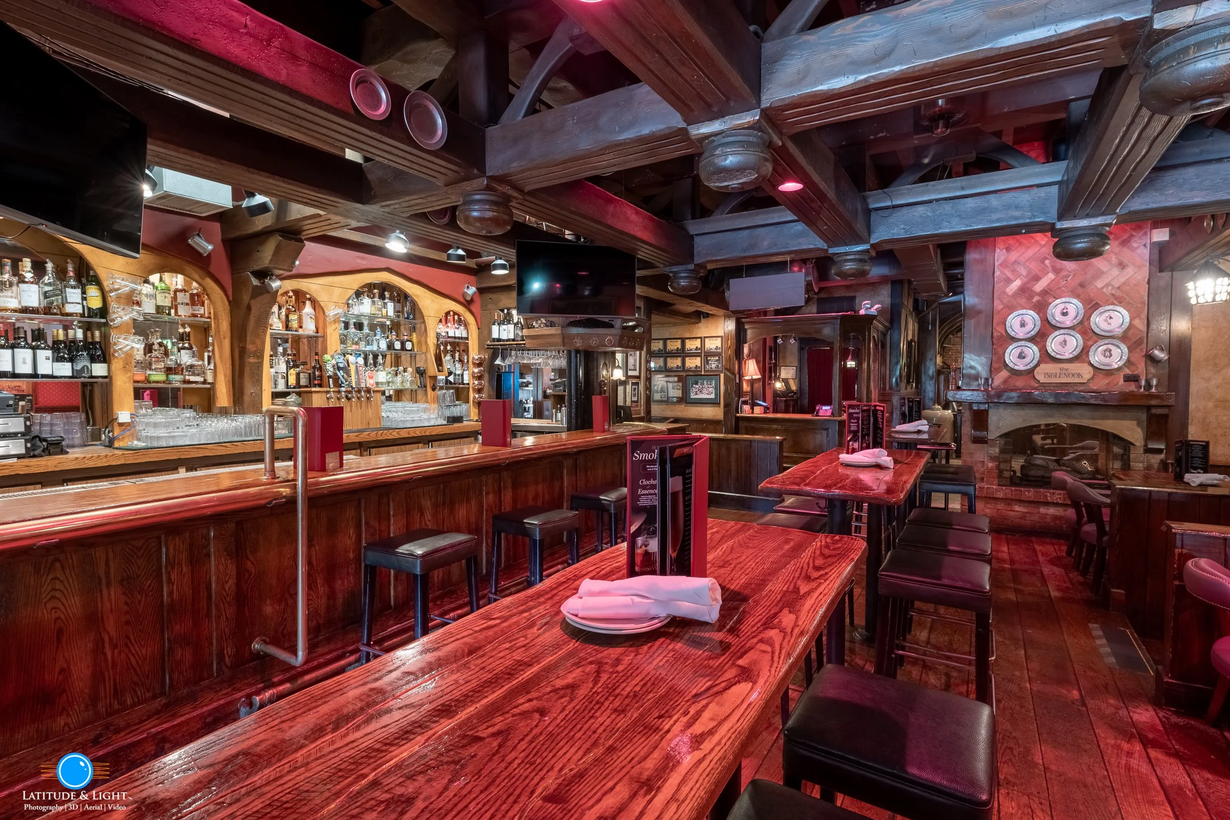 Interior view of a cozy, rustic bar and restaurant in Spokane with wooden tables, chairs, and a fireplace, featuring a bar with bottles and glasses.