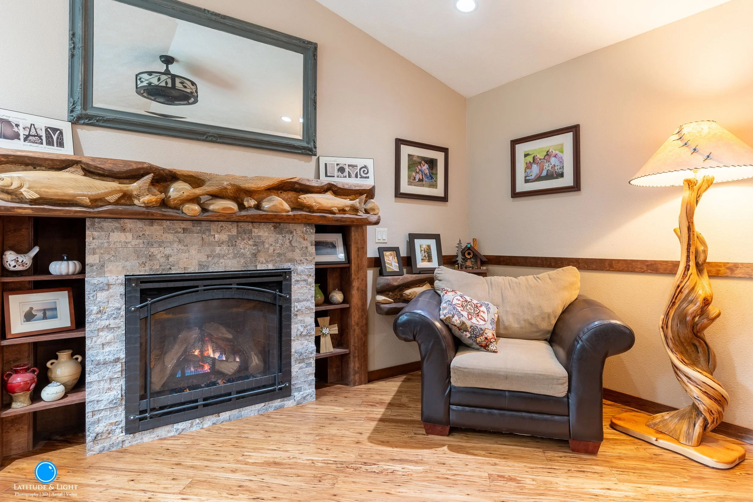 Cozy living room in North Idaho with a stone fireplace, framed family photographs, decorative items, a leather and fabric armchair with a patterned cushion, and a distinctive wooden floor lamp.