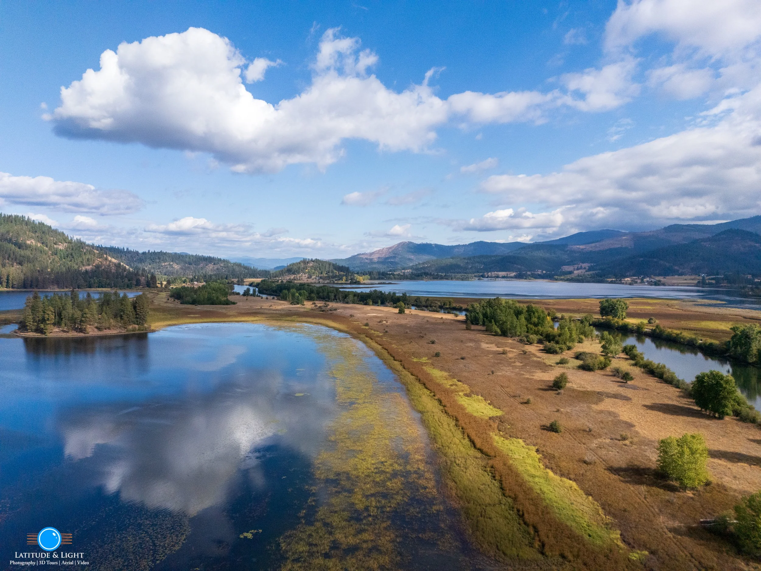 Harrison, Idaho: Aerial view of a landscape with lakes, grassy fields, trees, hills, and mountains under a partly cloudy sky.