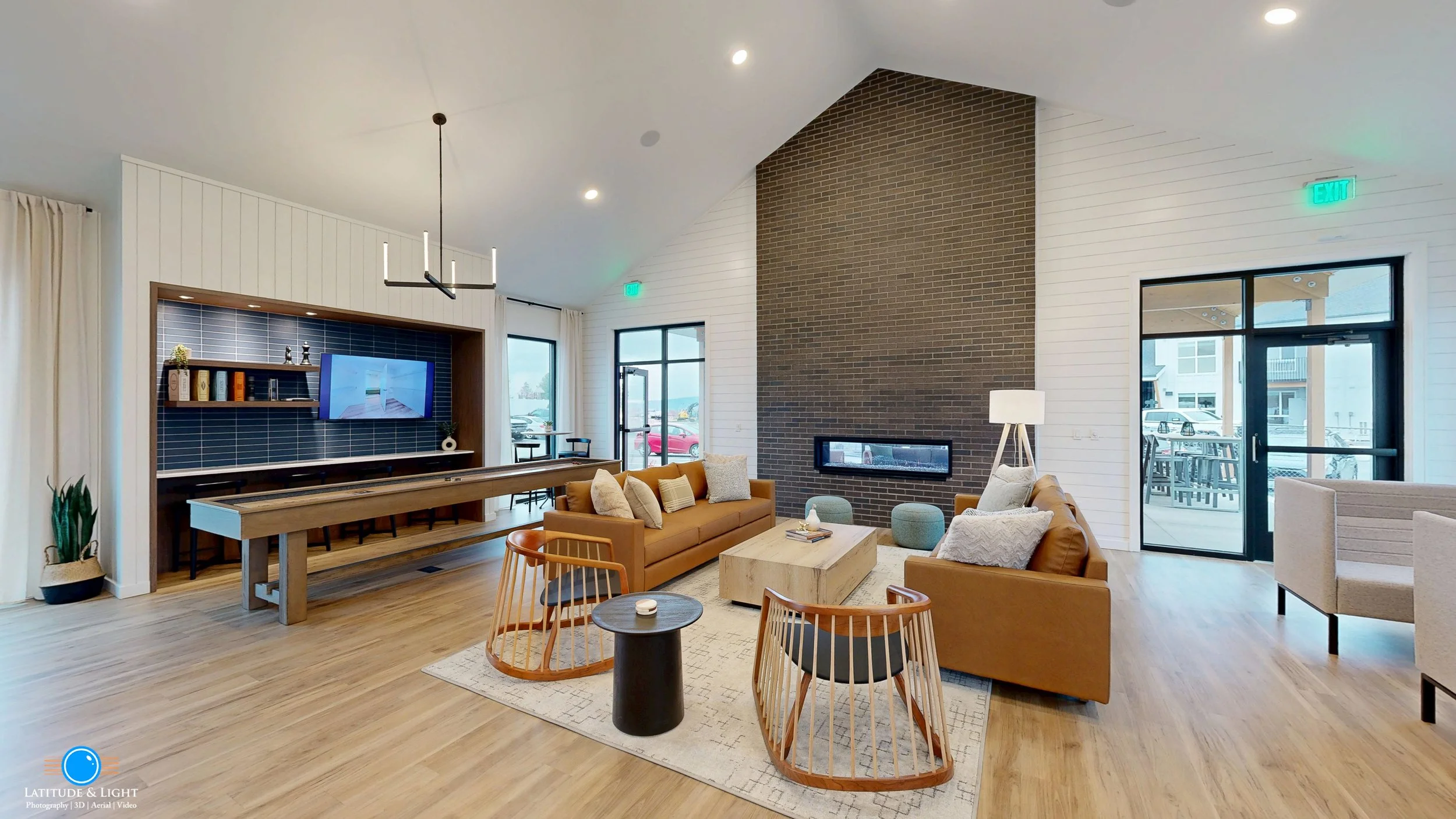 A Spokane Valley area apartment community center with two brown sofas, a marble coffee table, wooden chairs with black cushions, set on a cream rug. A wood-paneled wall with a fireplace and a large window are in the background.