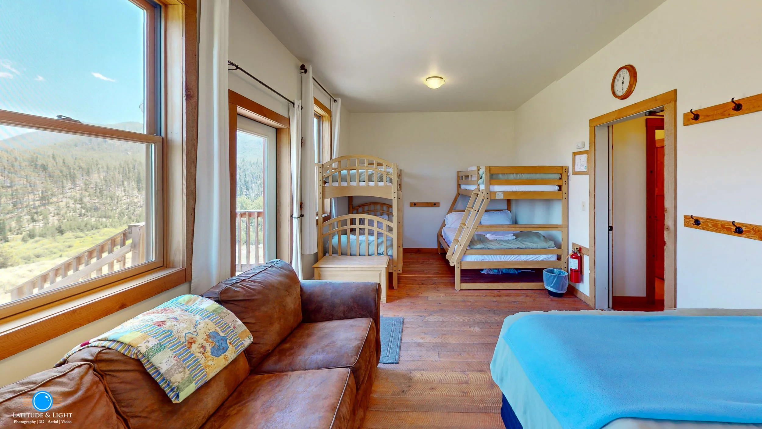 Room with multiple bunk beds, a leather sofa, and large windows showing mountain scenery.