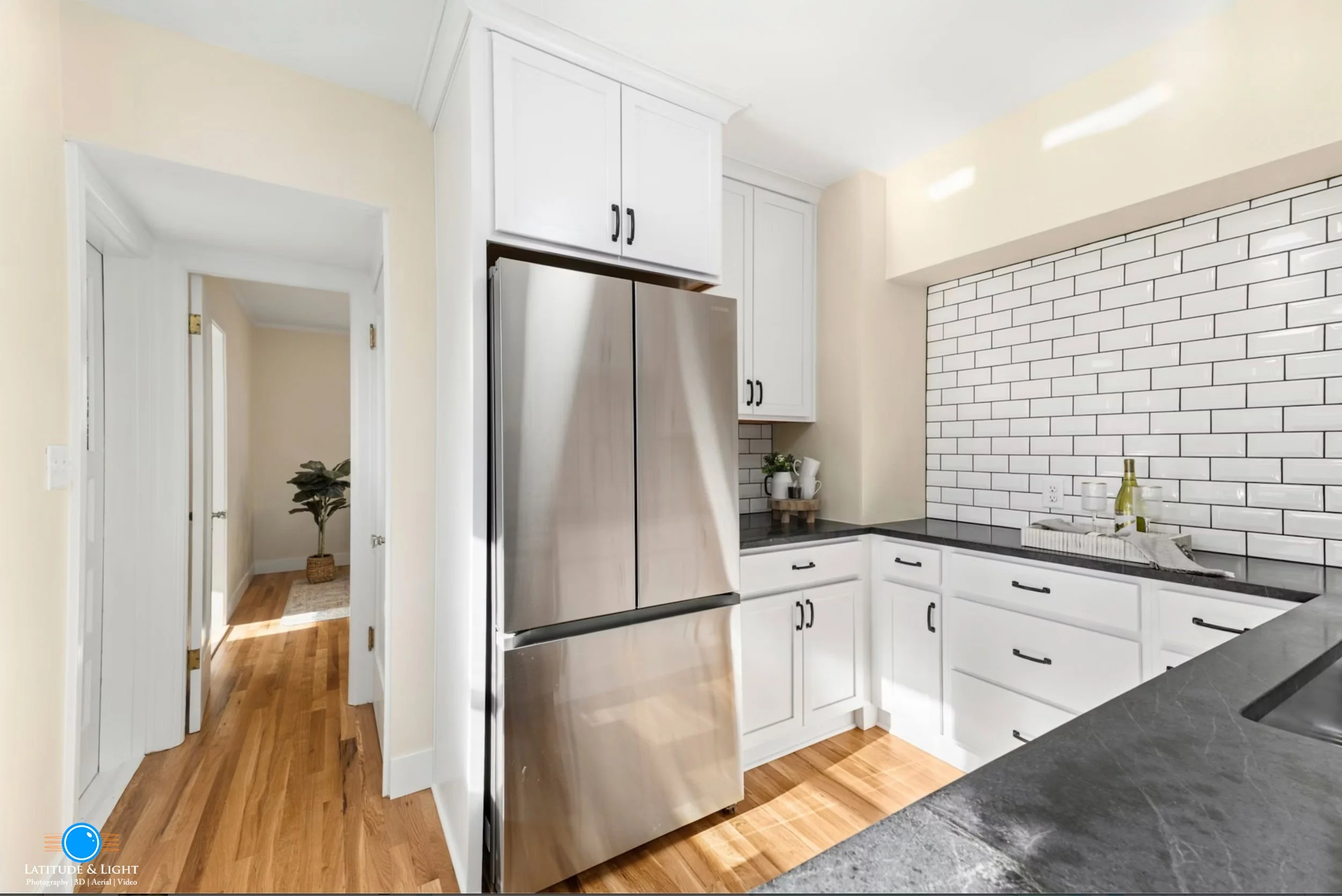 Modern kitchen with white cabinets, black countertops, stainless steel fridge, and white subway tile backsplash.