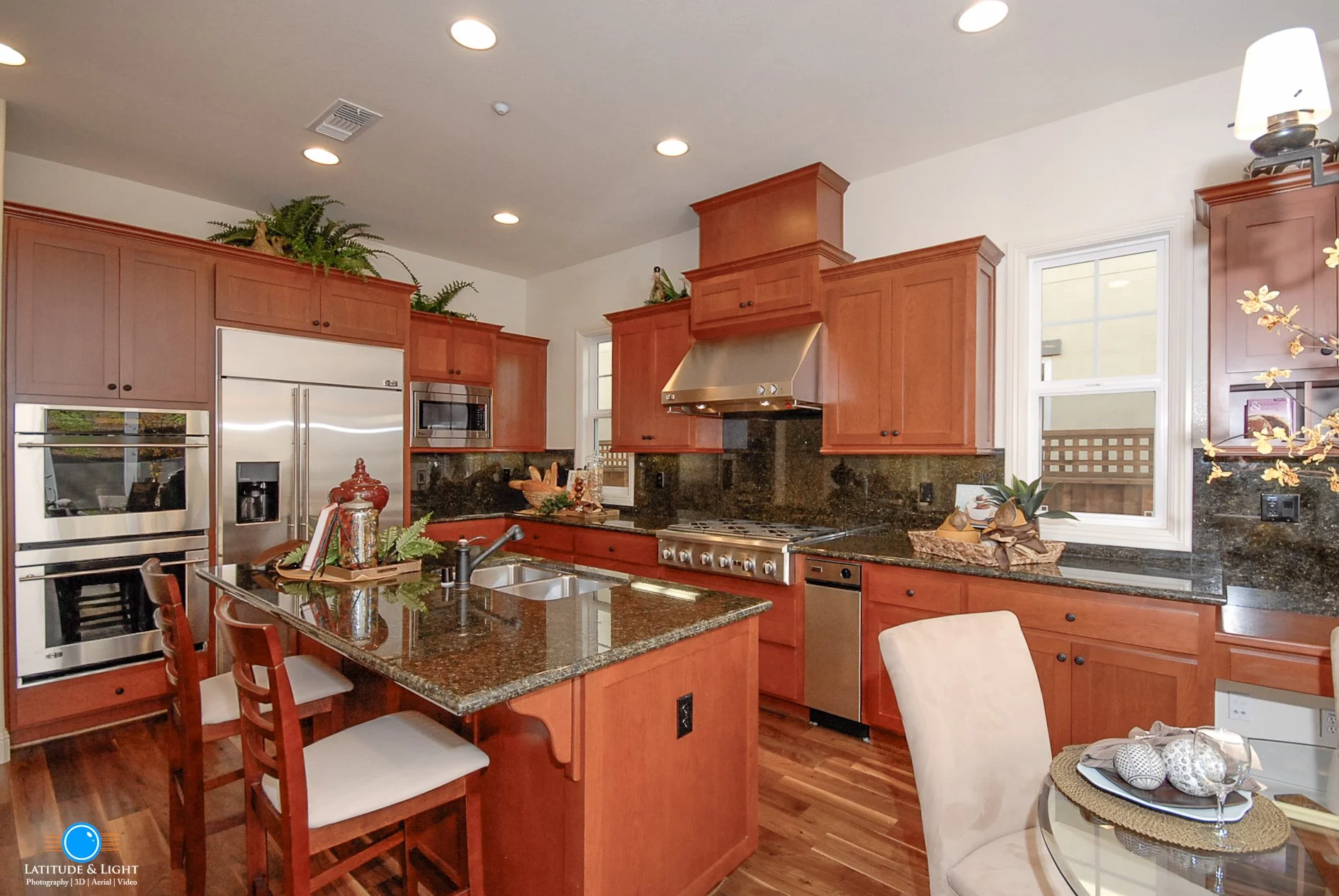 Kitchen with wooden cabinetry, granite countertops, stainless steel appliances, and a small breakfast bar with three chairs.