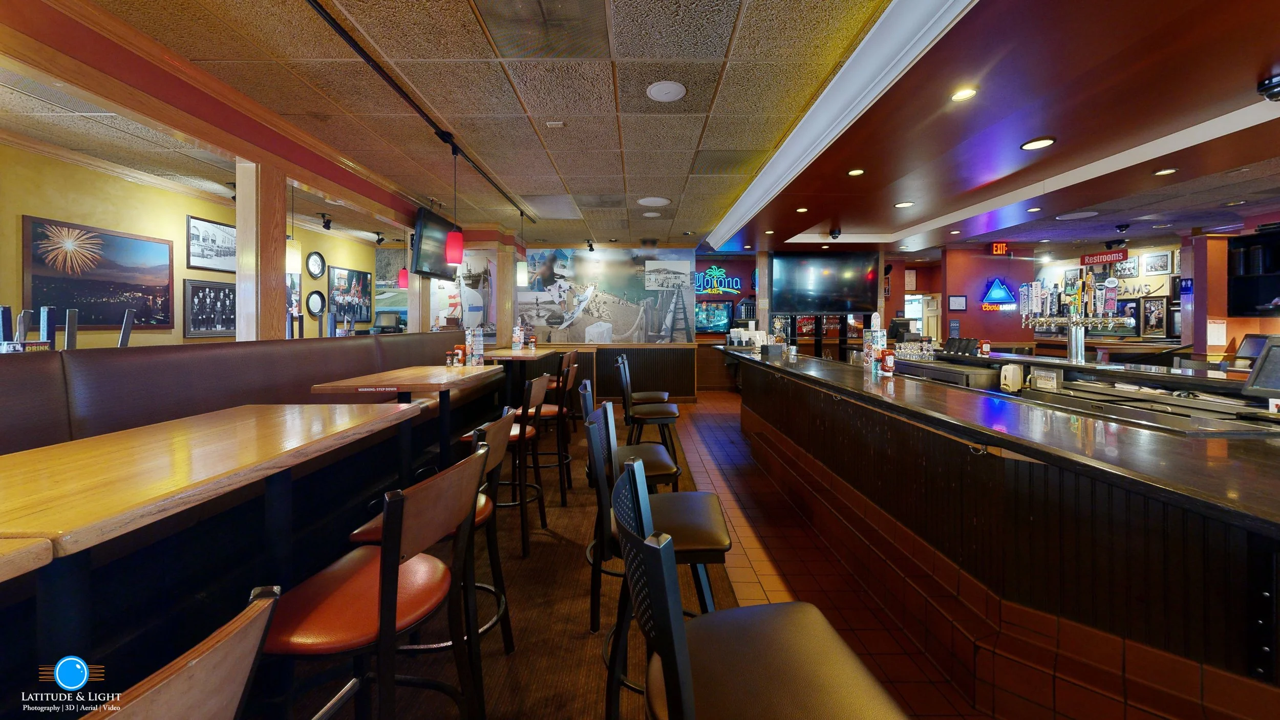 Empty bar and seating area in a casual restaurant and sports bar in Kennewick, with televisions, photographs, and neon signs on the walls.