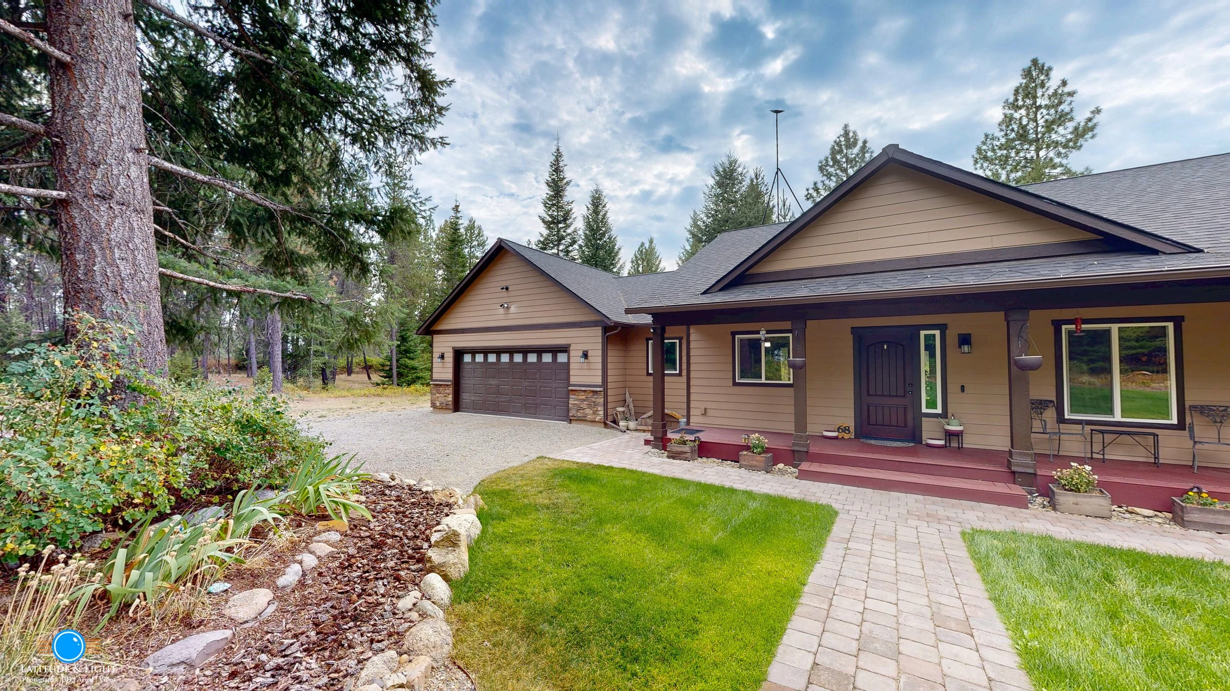 A suburban house with a brown garage door, front porch with steps, and landscaped yard, surrounded by trees under a cloudy sky.