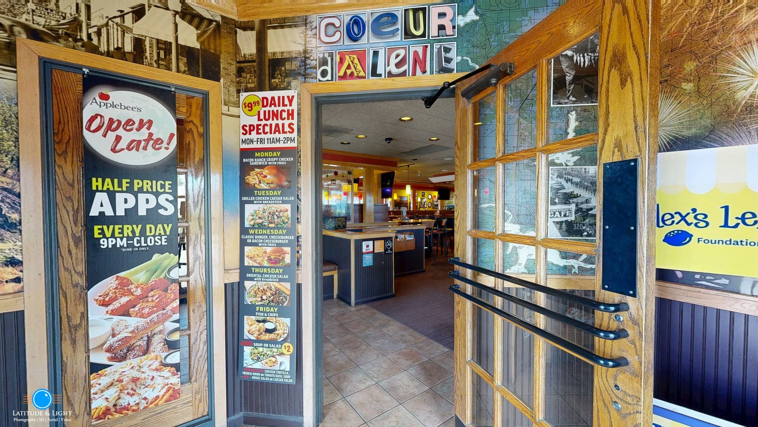 Entrance to an Applebee's restaurant with promotional signs advertising daily lunch specials, half-price apps every day from 9 PM to close, and the restaurant's interior visible through the doorway.
