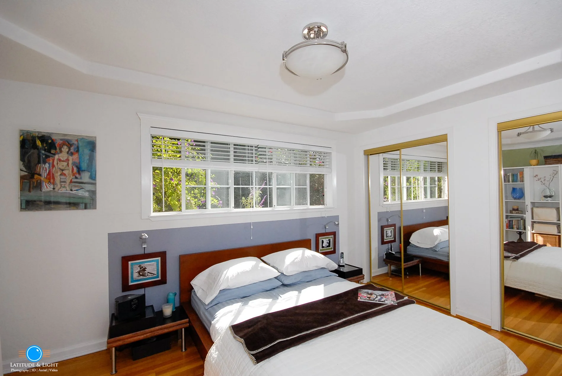 North Idaho bedroom with a large window, a bed, mirrored closet doors, and a bookshelf in the corner.