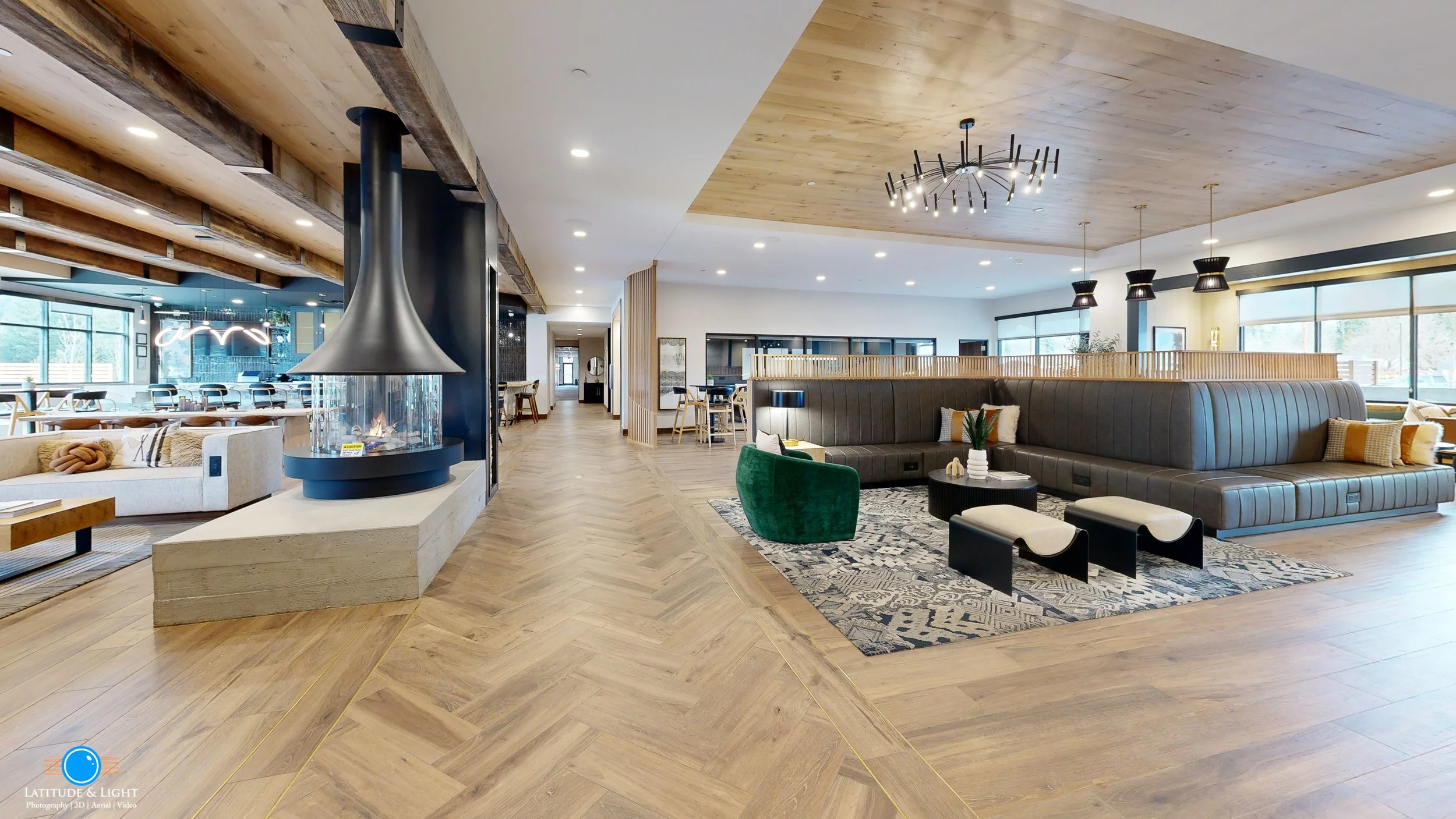 Modern hotel lobby in Sandpoint, Idaho with wooden flooring, a fireplace, a large curved leather sofa, a green accent chair, and contemporary ceiling lights.
