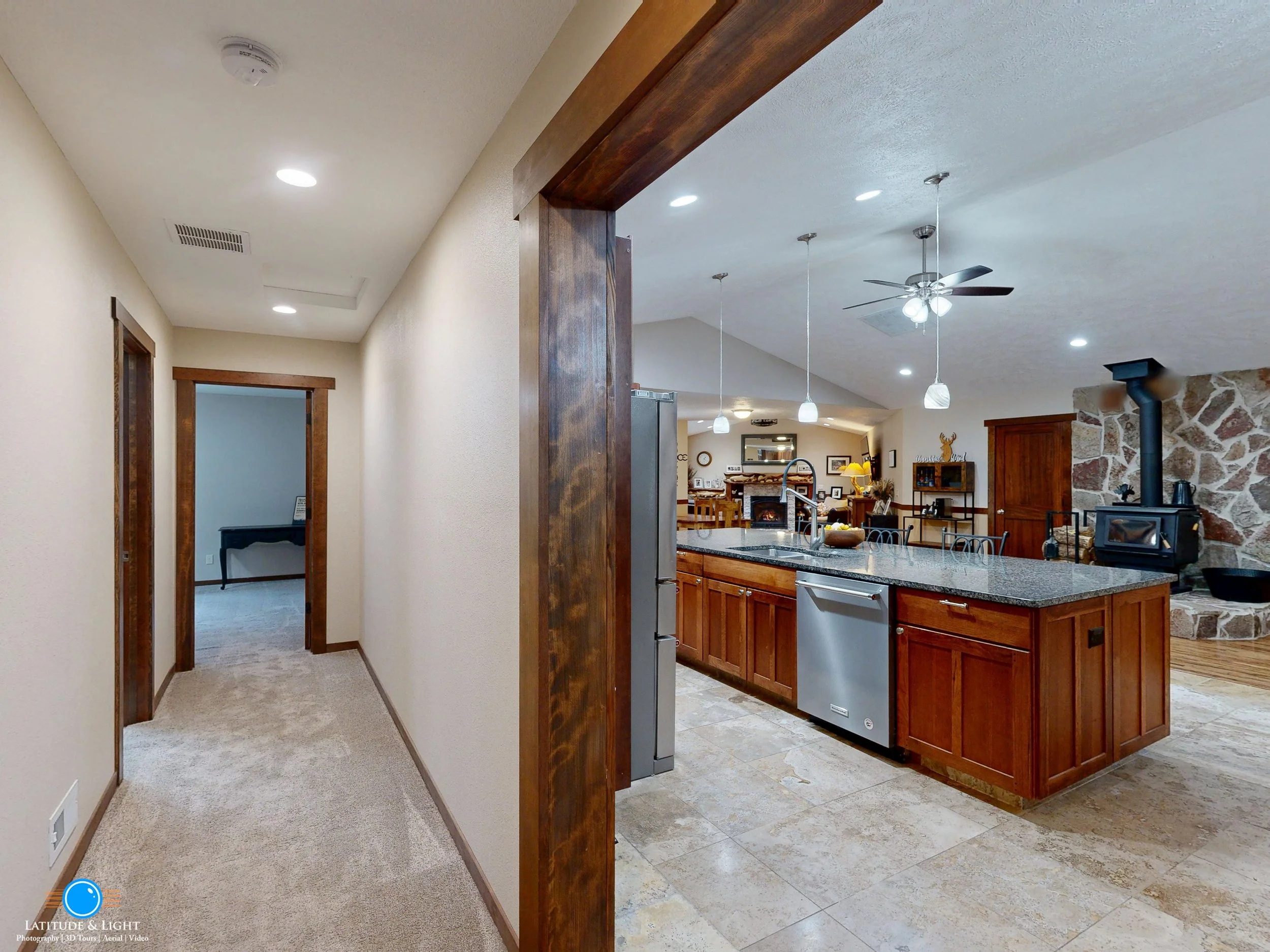 Coeur D'Alene: View of a hallway leading into an open-concept kitchen and living area with wooden accents, a stone fireplace, and modern decor.