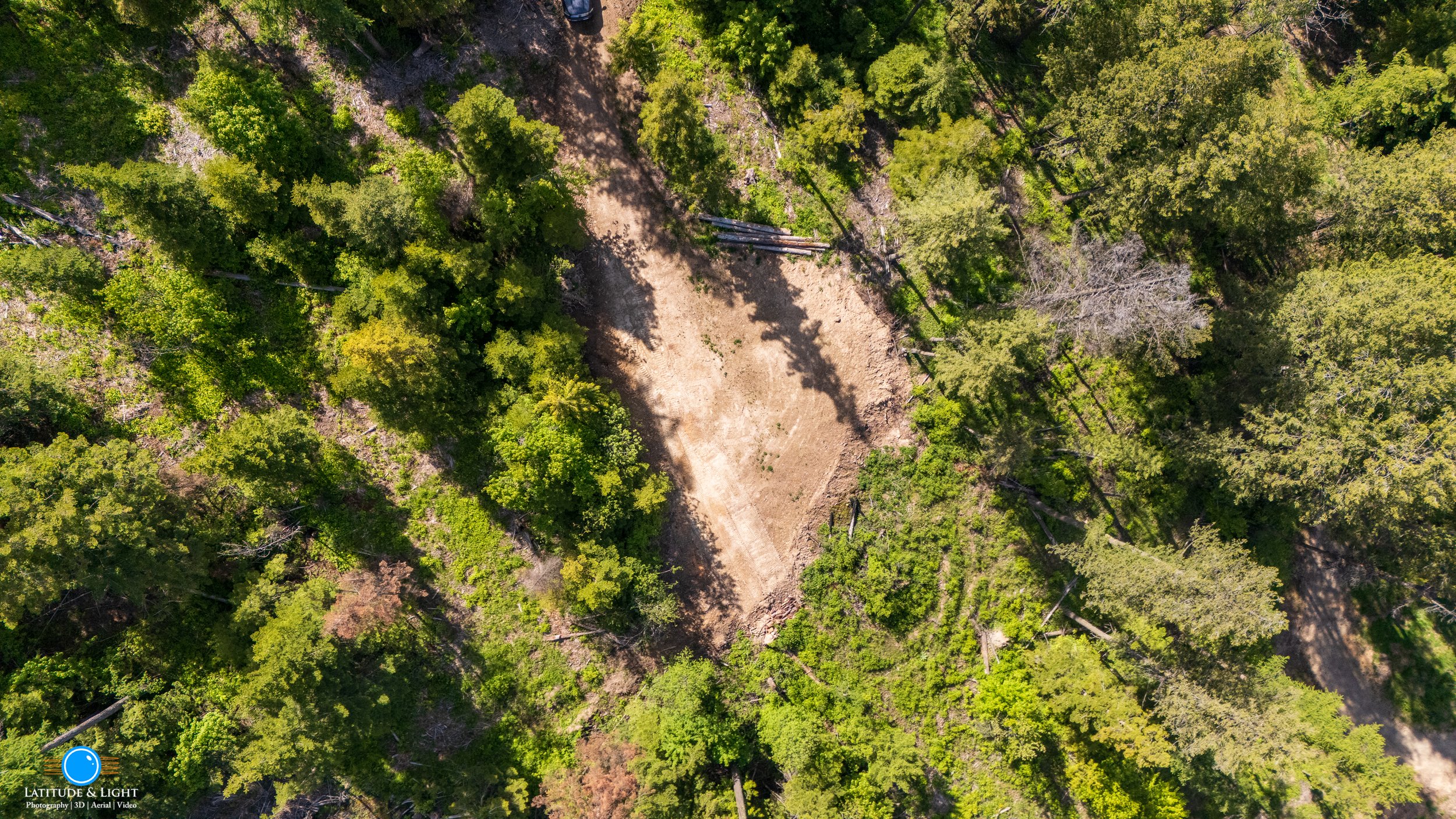 Land in Harrison, Idaho: Aerial view of a dirt path in a green forest with trees casting shadows over the ground.