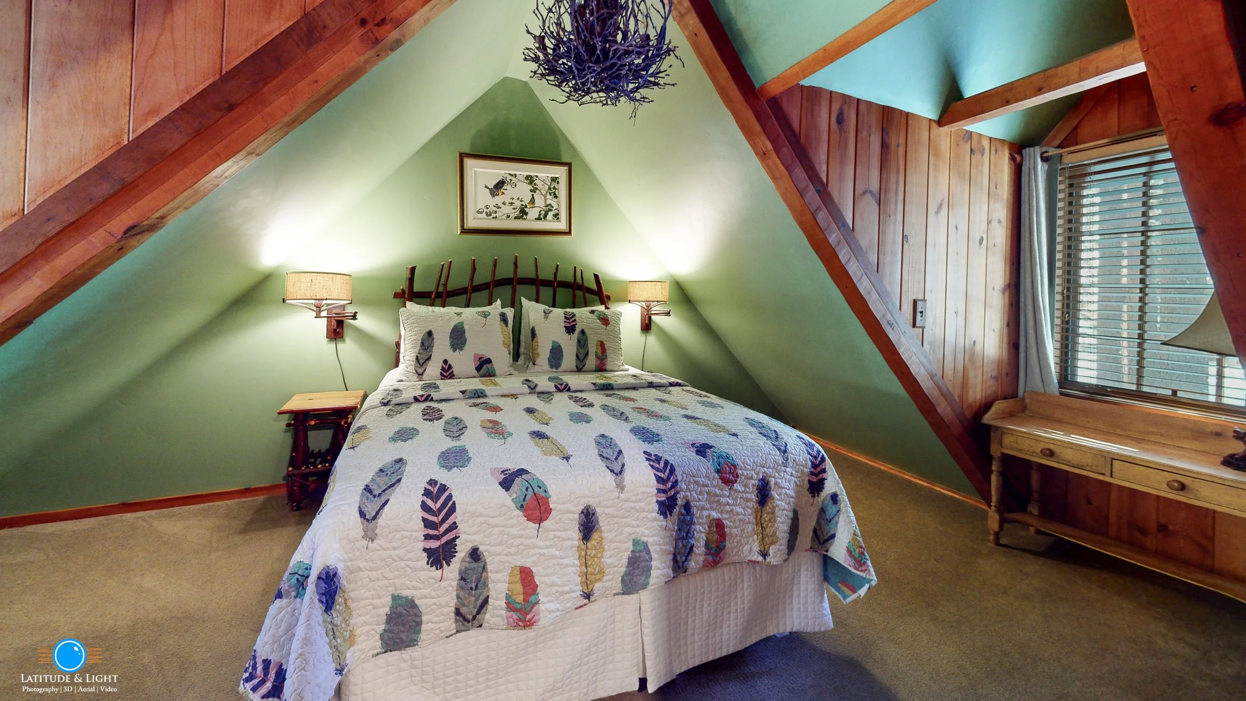 Cozy bedroom with a bed featuring a feather-patterned quilt, green walls, wood accents, and a small window with blinds.