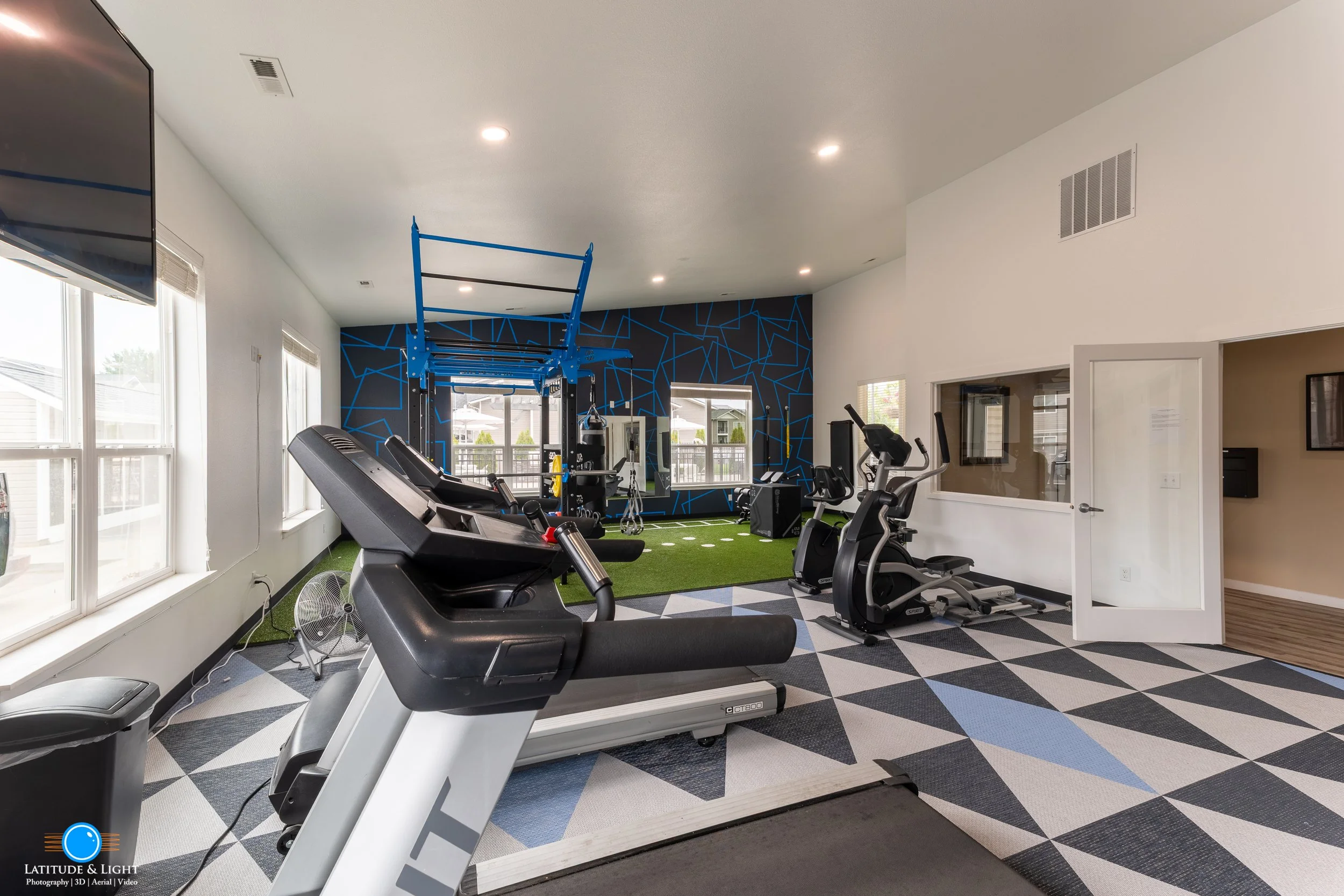 Modern indoor gym at a Liberty Lake apartment community center with treadmills, stationary bikes, a pull-up rig, and a wall with geometric blue patterns.