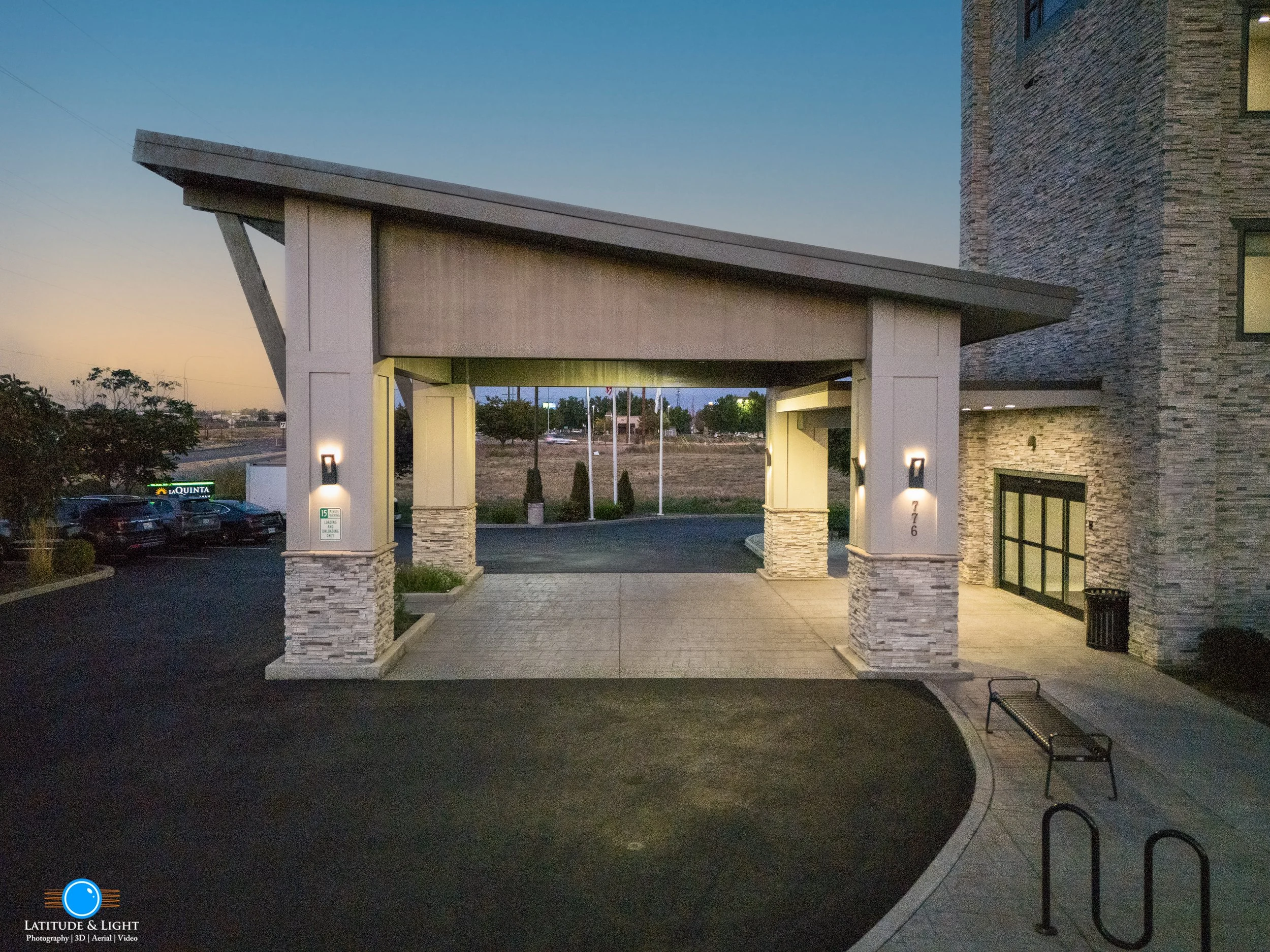 LaQuinta Inn by Wyndham entrance with a covered driveway, stone accents on the pillars, and parking lot in the background during dusk.