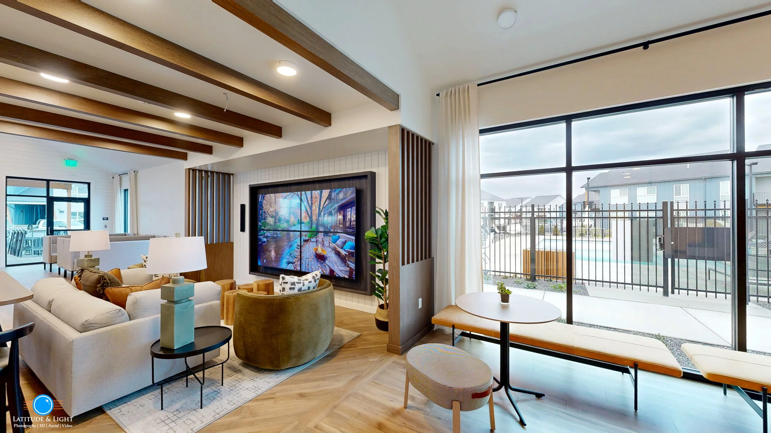 Interior of a Spokane Valley area apartment community center with a large window, white walls, wooden ceiling beams, a TV, and seating area.