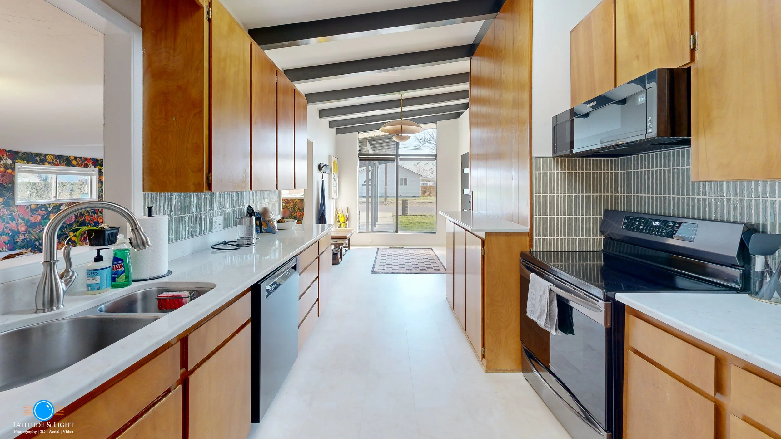 Modern kitchen with wooden cabinets, white countertops, black appliances, and a window overlooking the backyard.