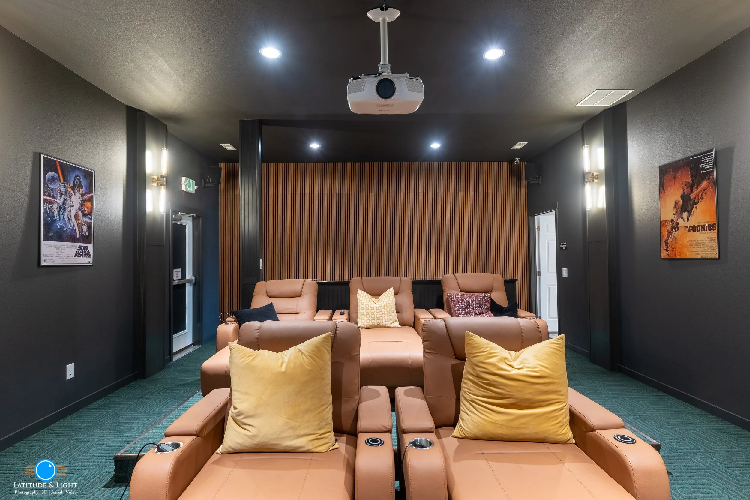 At an apartment complex near Spokane, a Home theater room with leather recliners, a projector mounted on the ceiling, movie posters on dark walls, and a wooden accent wall.