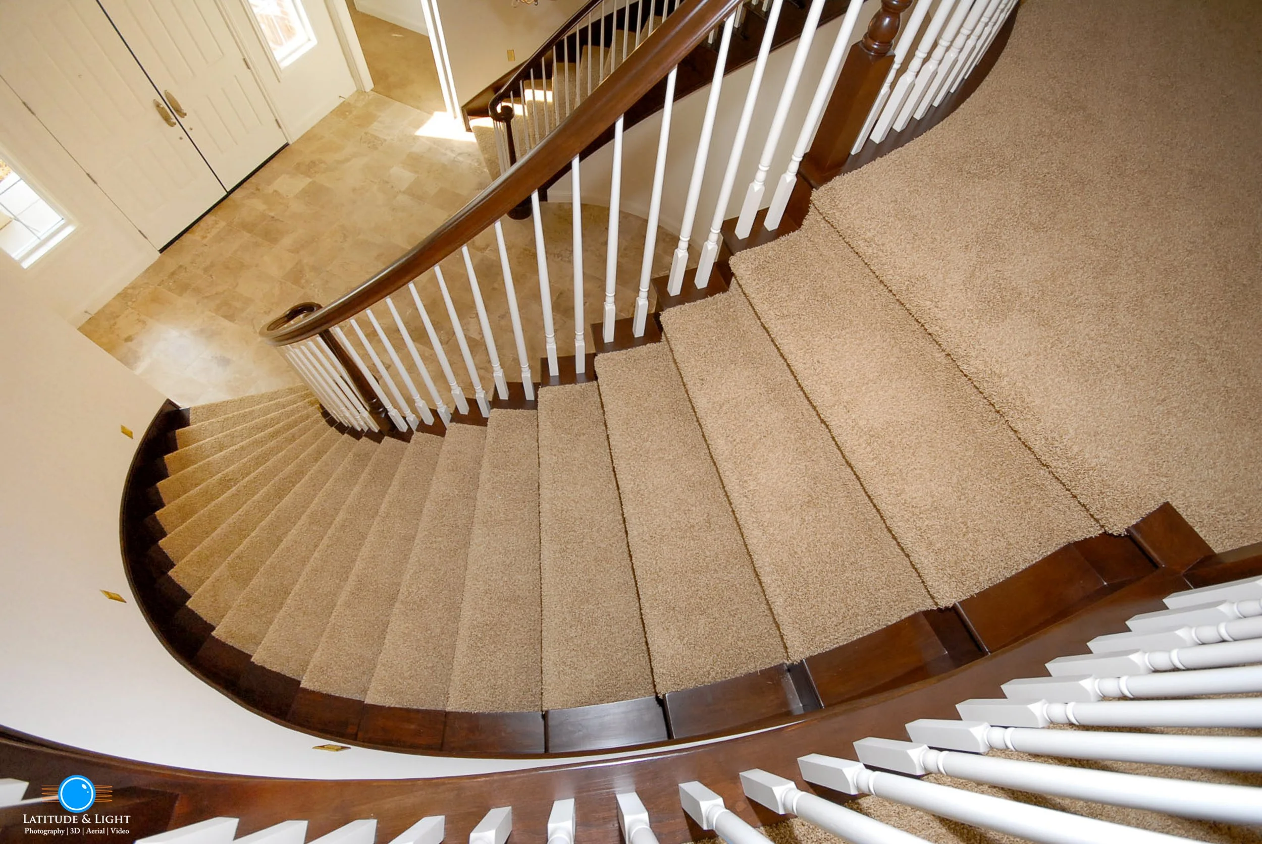 Coeur D'Alene: A view of curved staircase from top, showing beige carpeted steps with white spindles and wooden handrail, leading to a beige tiled foyer.