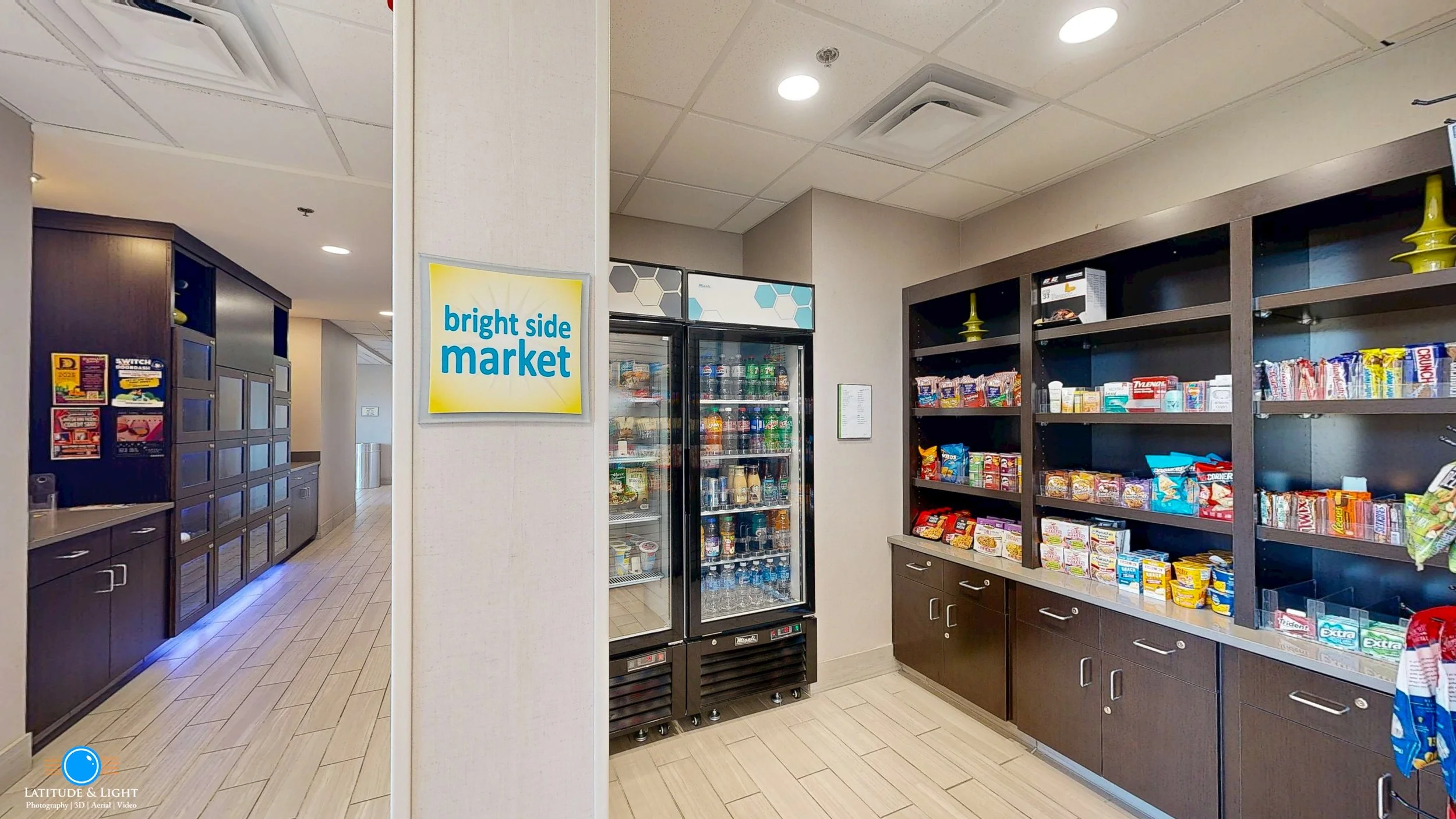 LaQuinta Inn by Wyndham in Walla Walla's convenience store with a sign reading 'bright side market' next to a glass-front refrigerator stocked with drinks. Shelves hold snacks and packaged foods, with dark wood cabinetry below.