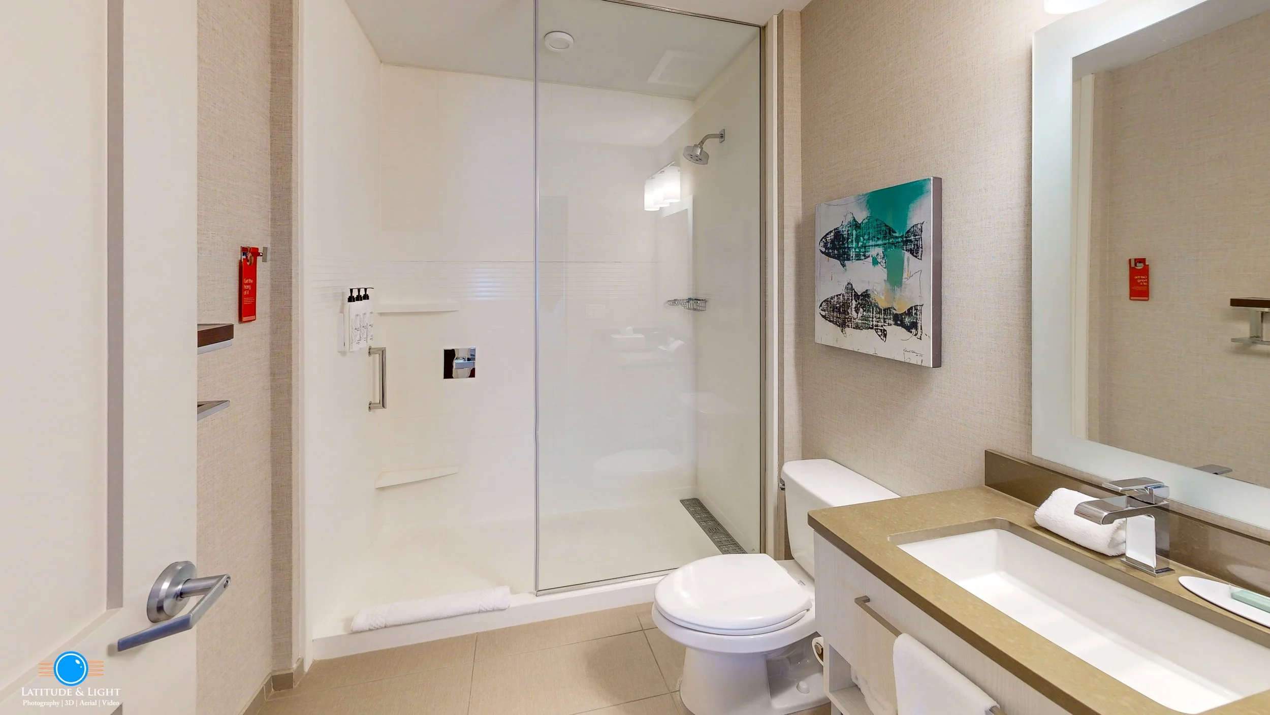 Modern hotel bathroom with walk-in shower, toilet, and vanity with mirror and sink.