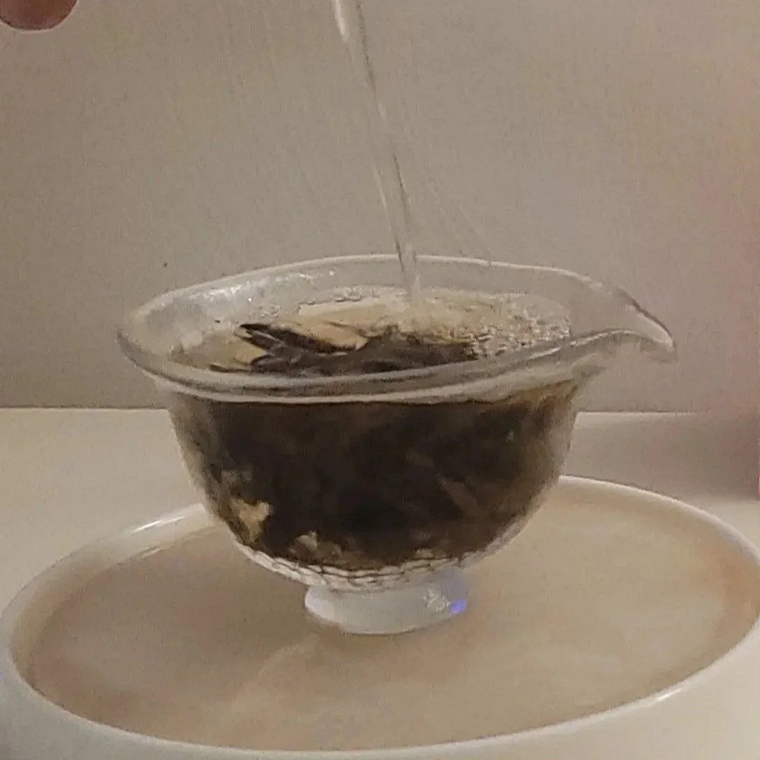 A glass bowl with a floral design on the rim is filled with water and placed above a beige circular container. Water is pouring into the bowl from above.