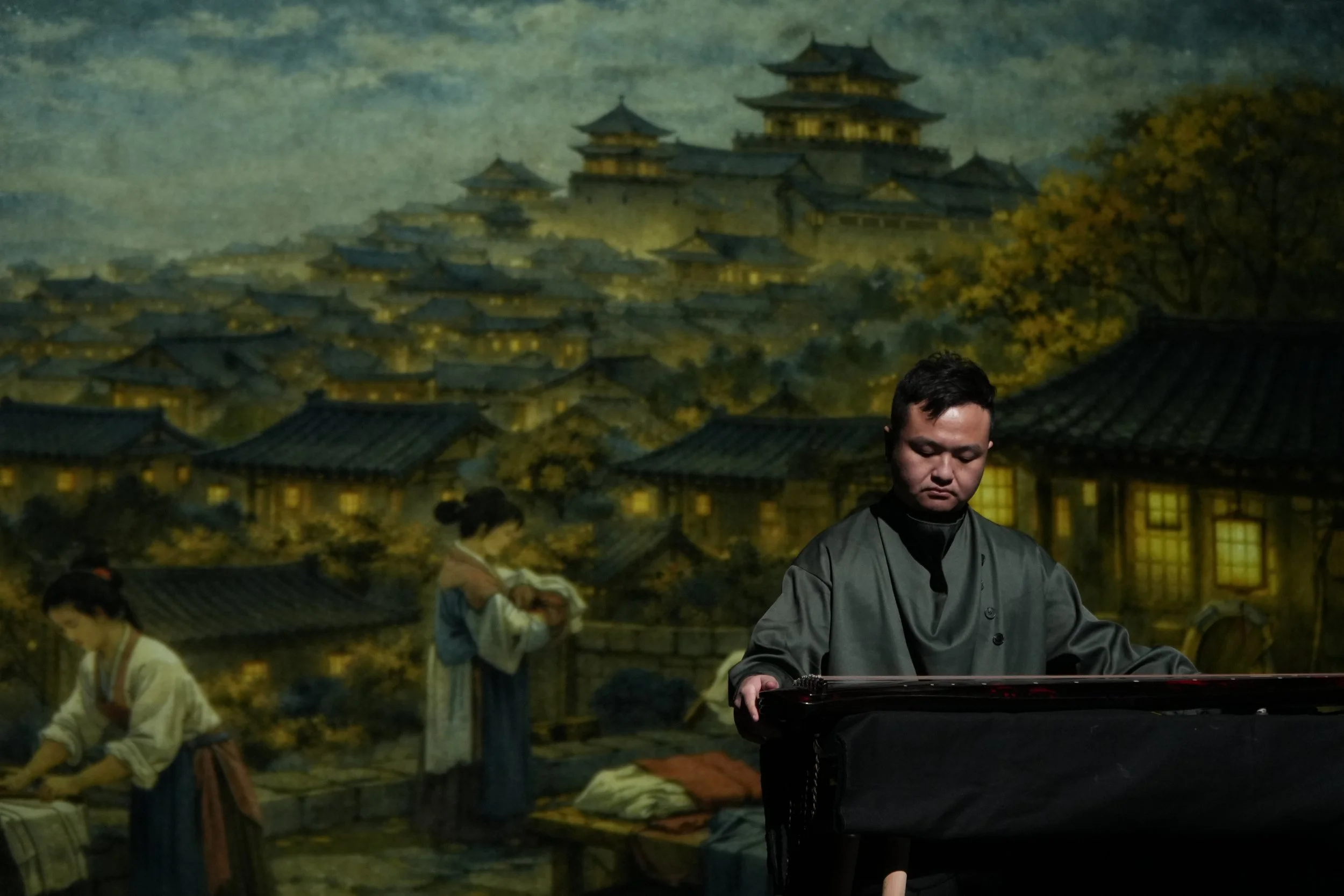 Atom Wang playing guqin in front of a traditional Asian village scene painting with buildings and women in traditional dress.