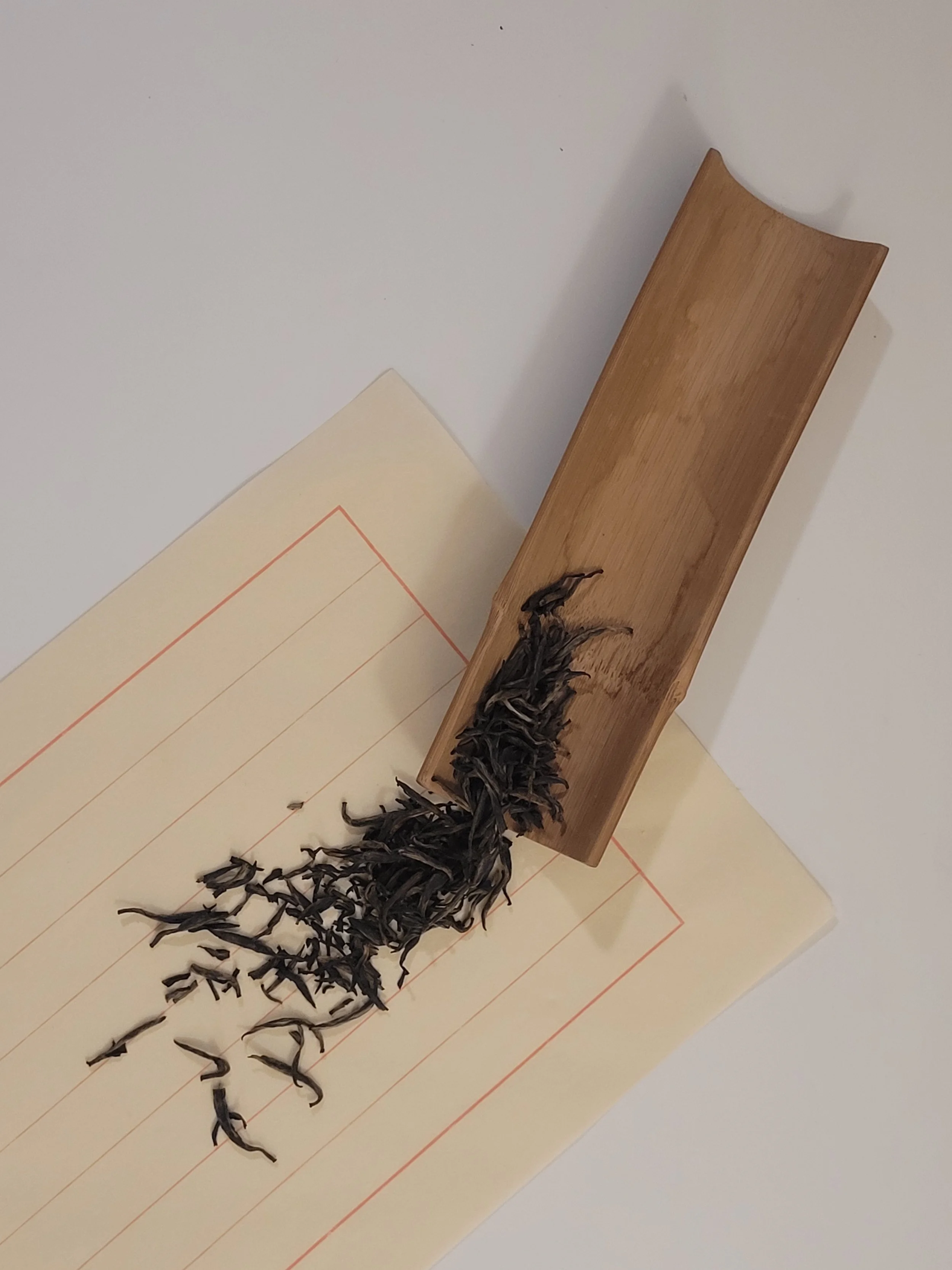 A wooden tray with dried black tea leaves on a lined piece of letter.