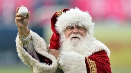 Santa Claus holding a baseball in his right hand outdoors.