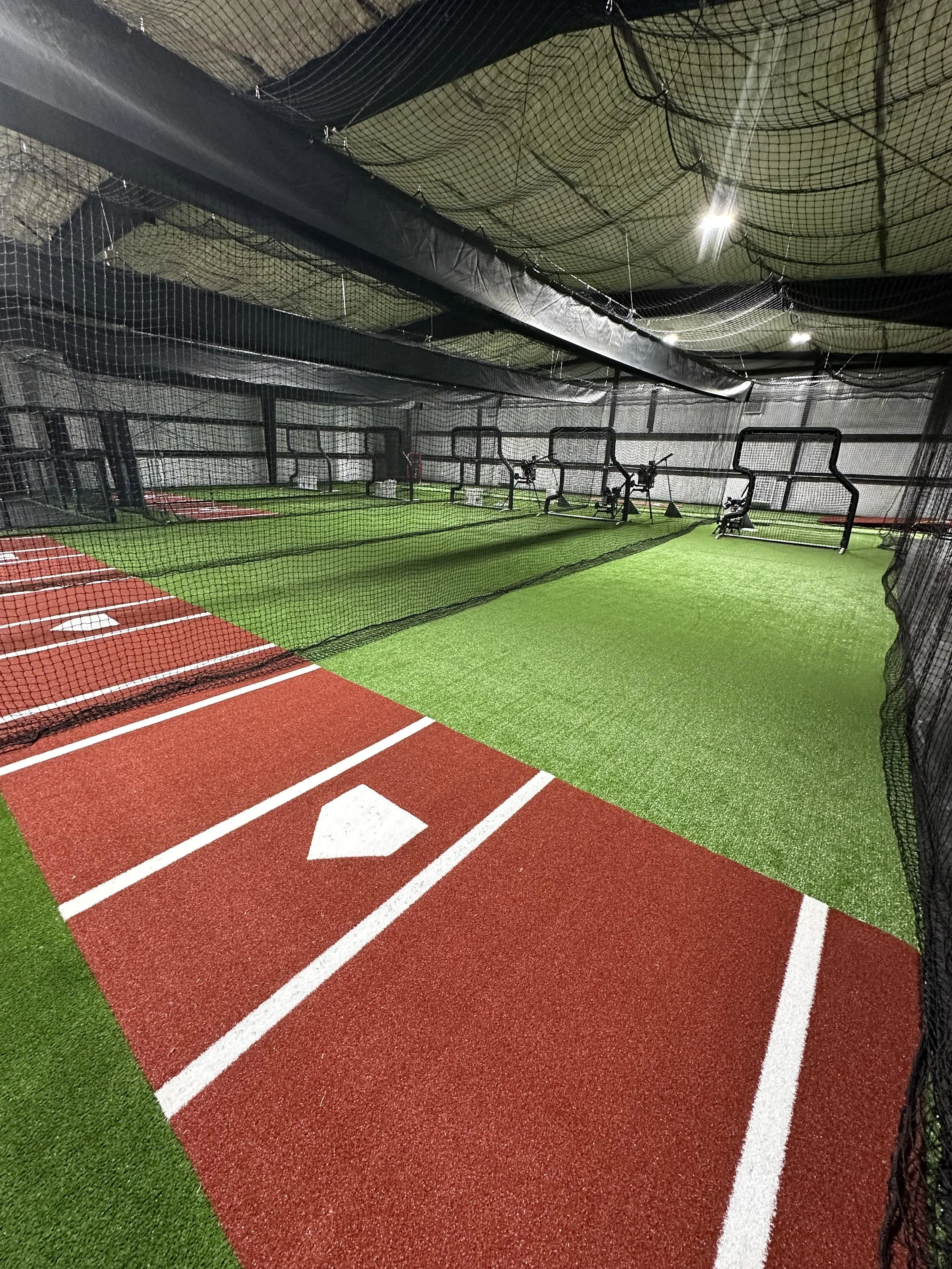 Indoor sports training area with artificial turf, batting cages with pitching machines, and a running track with lane markings.