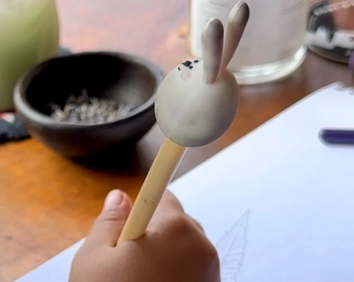 Una mano sostiene una cuchara que tiene una cereza hecha con material de papel o utensilio similar.