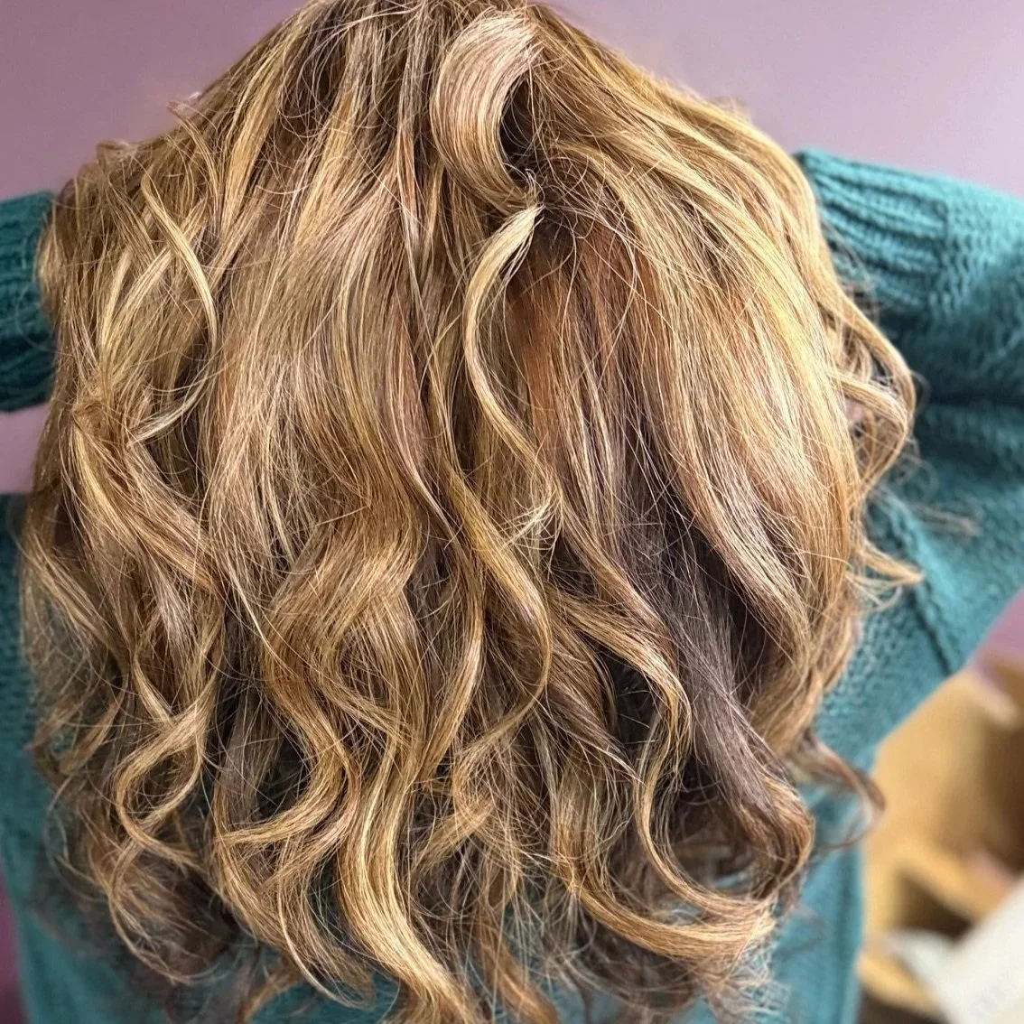 Close-up of wavy blonde hair styled with loose curls, seen from the back.