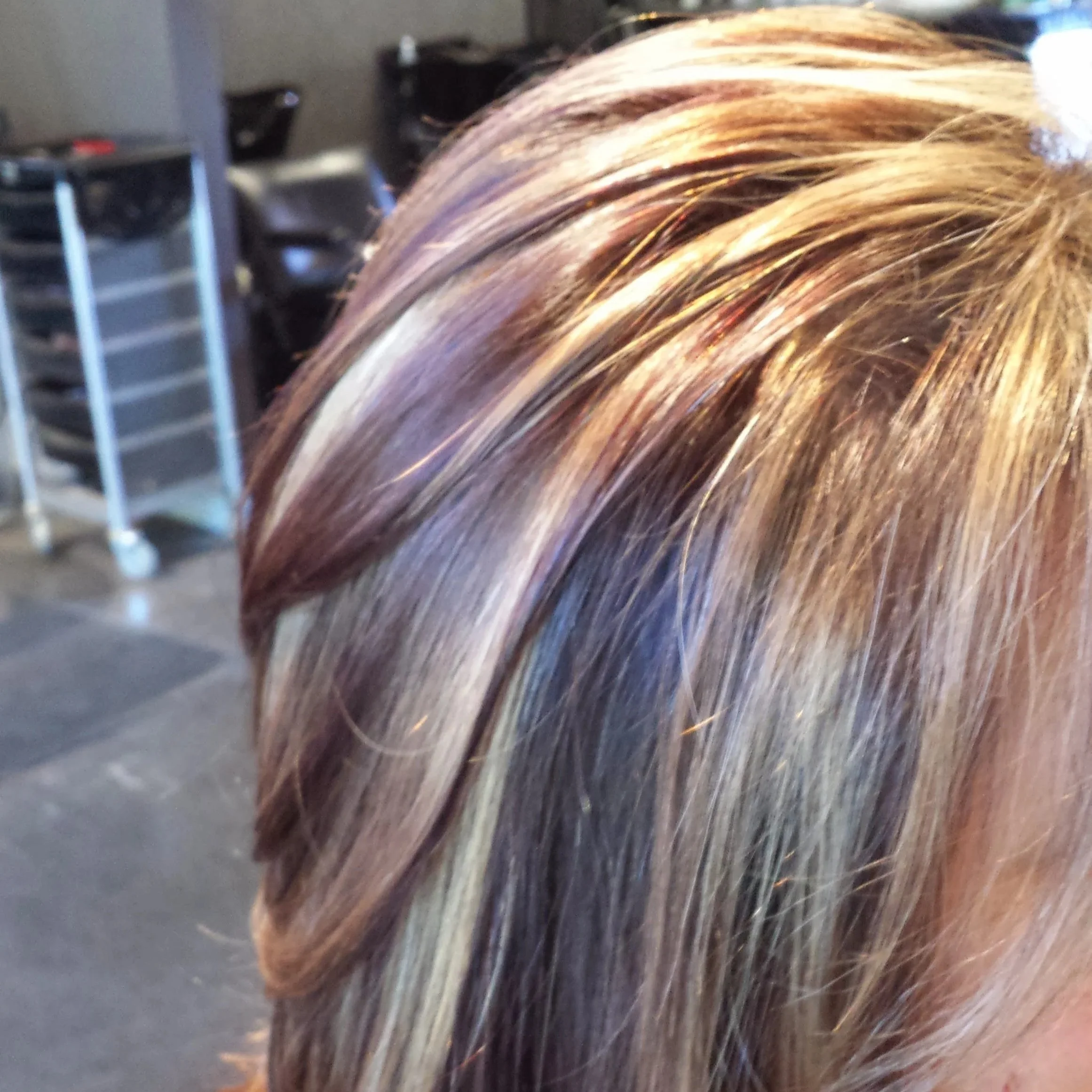 Close-up of a person's hair with blonde and light brown highlights, styled straight in a salon.