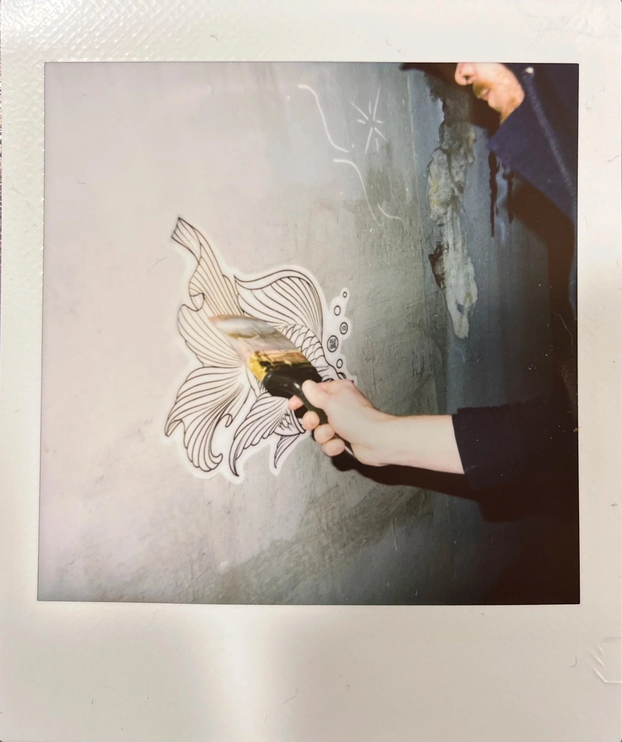 Person applying yellow paint to a fish illustration on a wall with a roller brush.