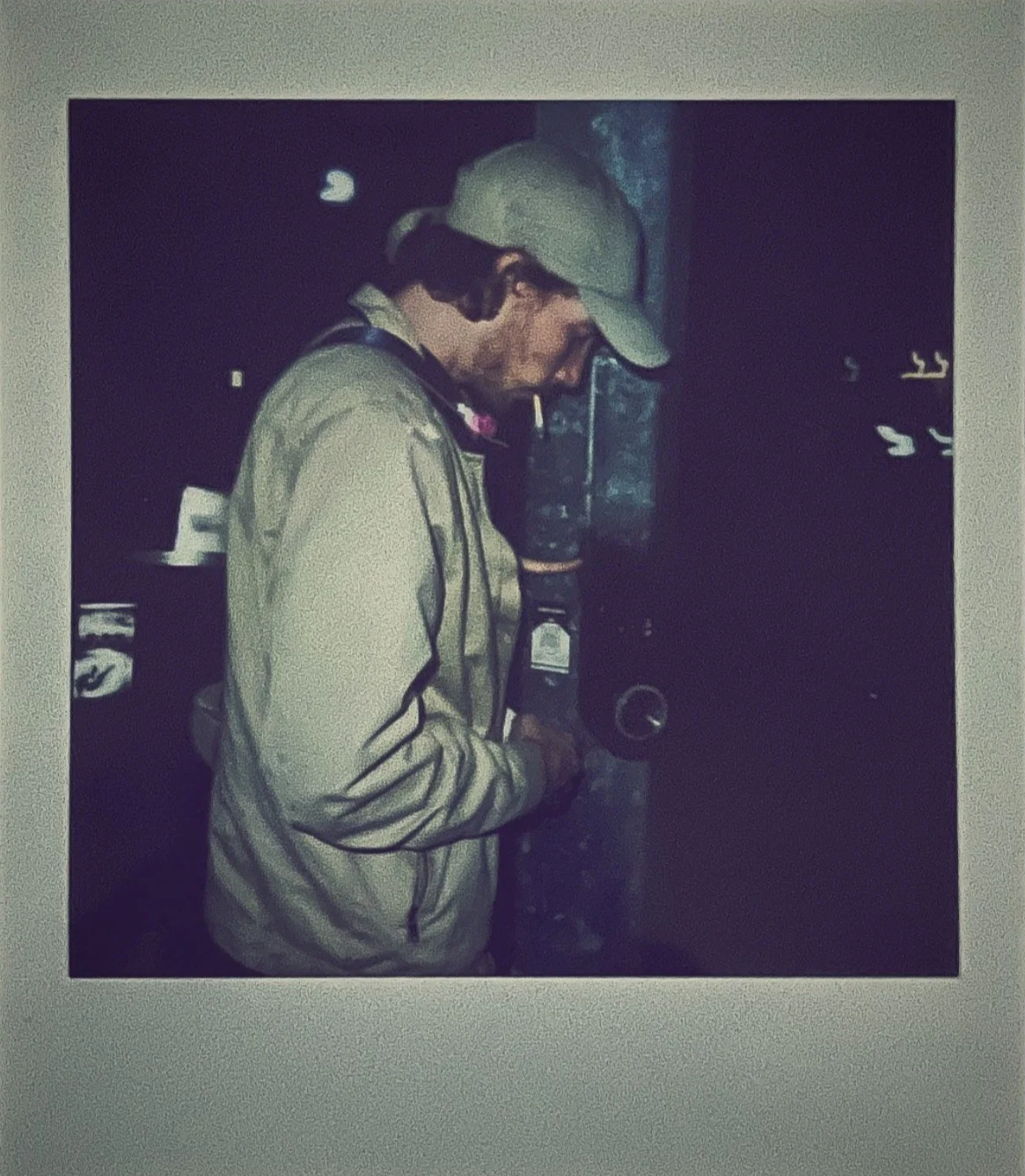 A man in a baseball cap and jacket standing outdoors at night, placing a sticker on a pole.
