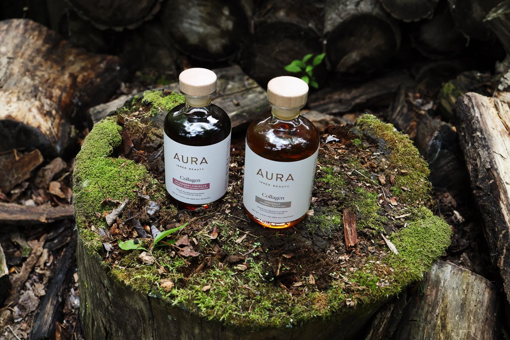 Two bottles of Aura Inner Beauty collagen supplements placed on a moss-covered tree stump in a forest setting.