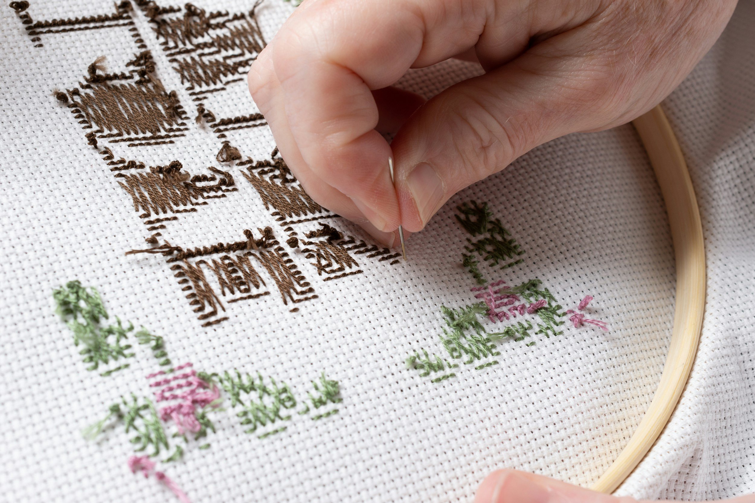 Close-up of a person cross-stitching a pattern onto white fabric using an embroidery hoop.