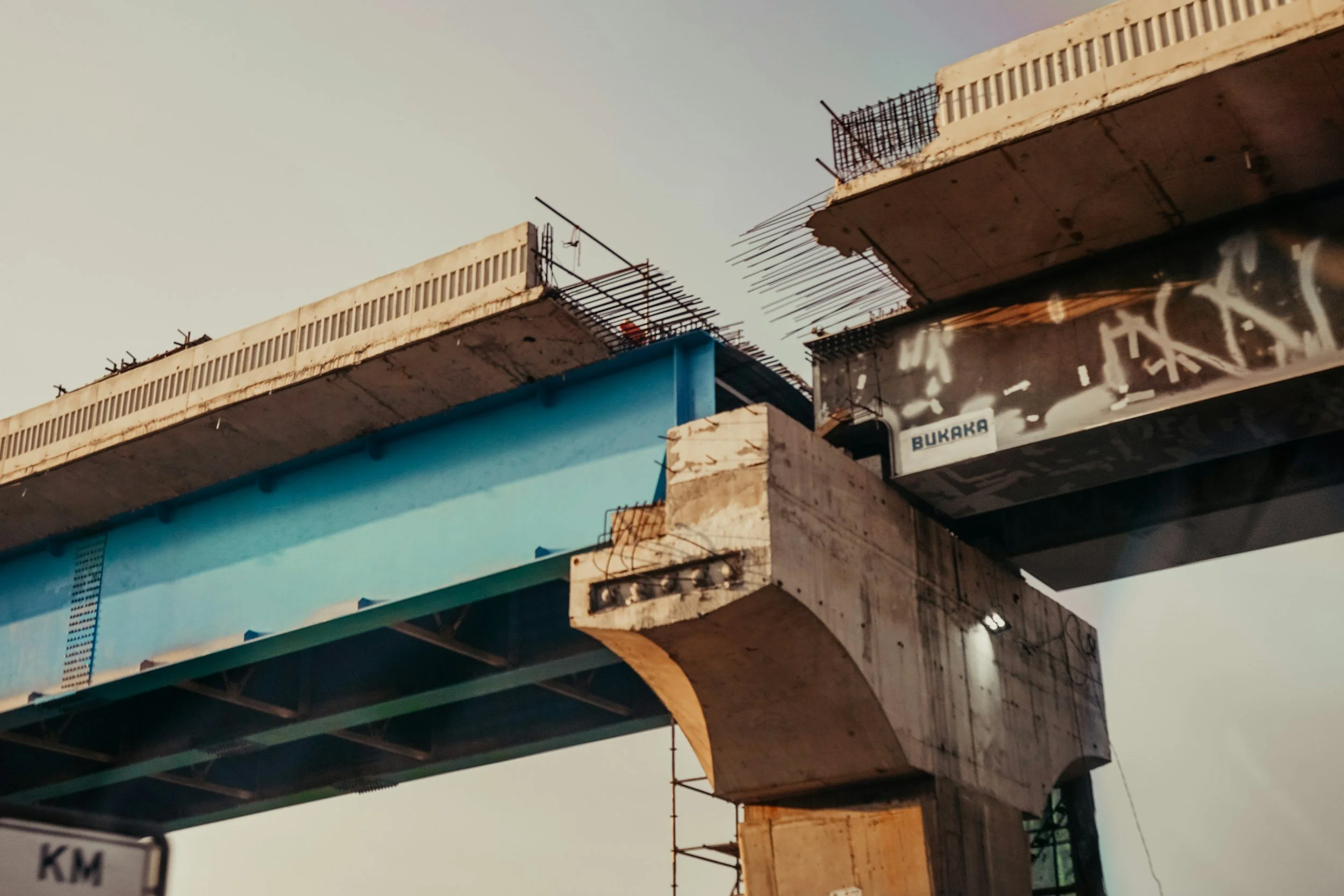 Close-up of a large multi-level concrete bridge under construction, with visible reinforcement bars and scaffolding.