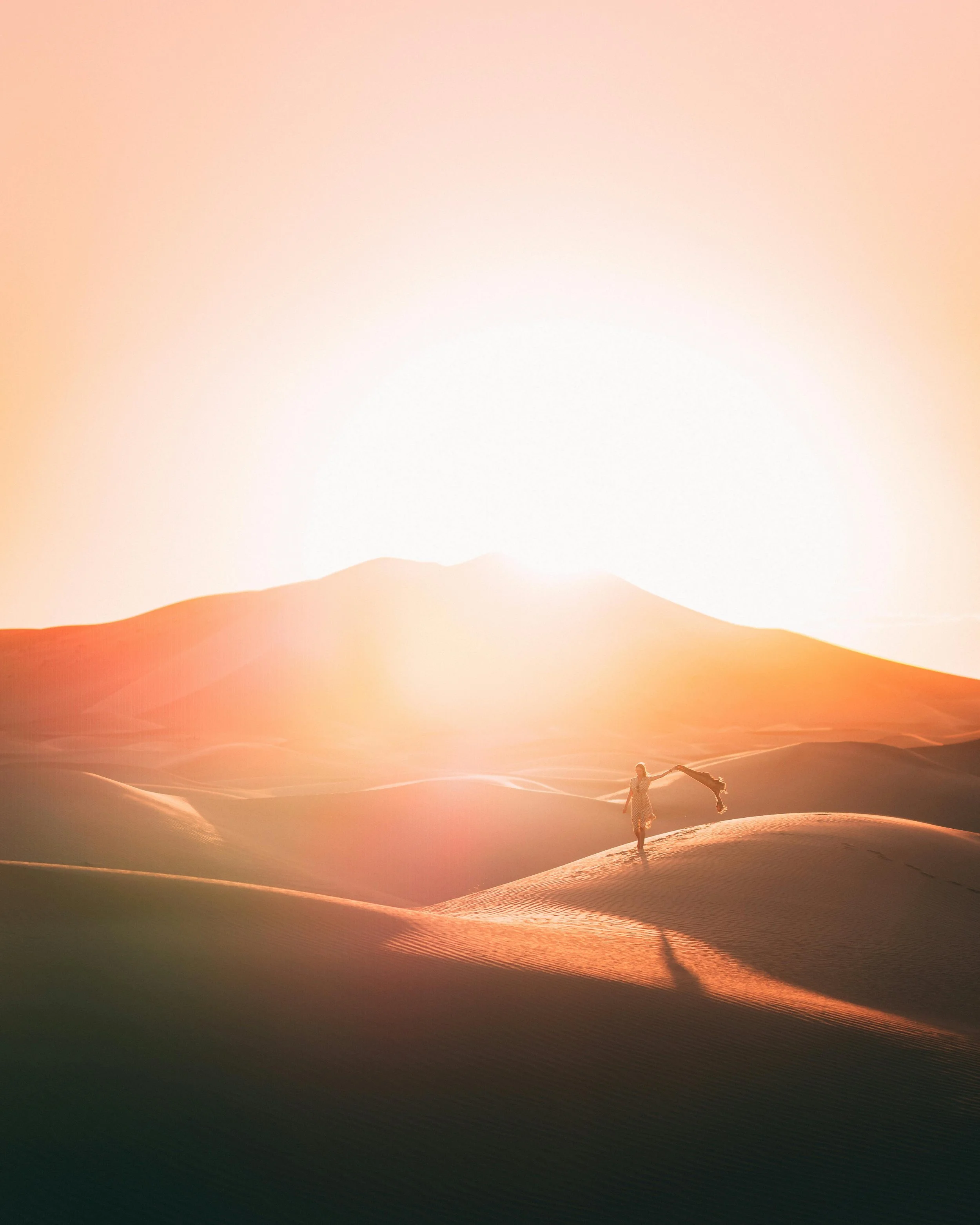 Person holding a scarf walking on sand dunes during sunset