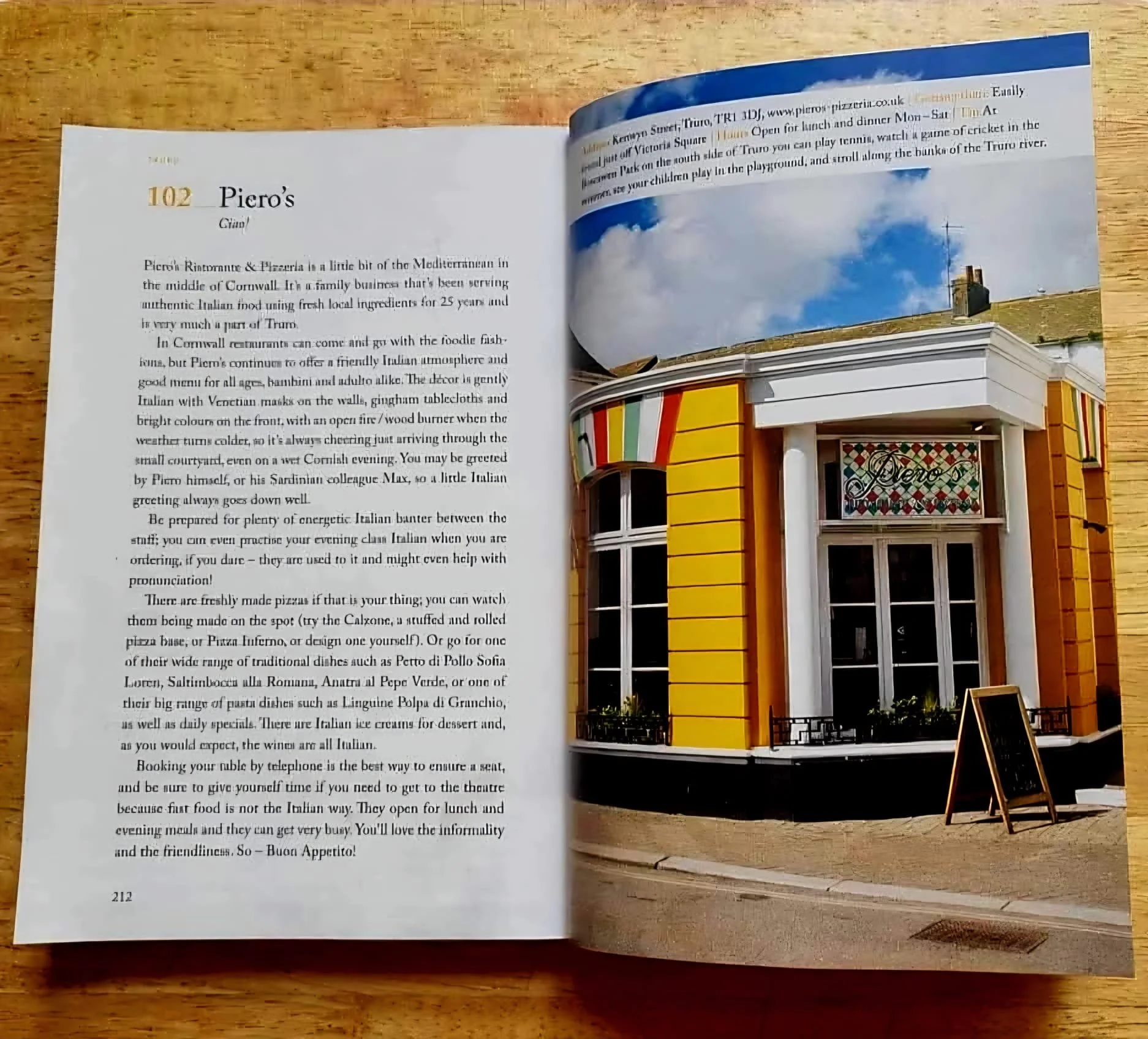 Open travel book showing a page about Piero's restaurant on the left and a photograph of a yellow storefront with white trim and an outdoor chalkboard sign on the right.