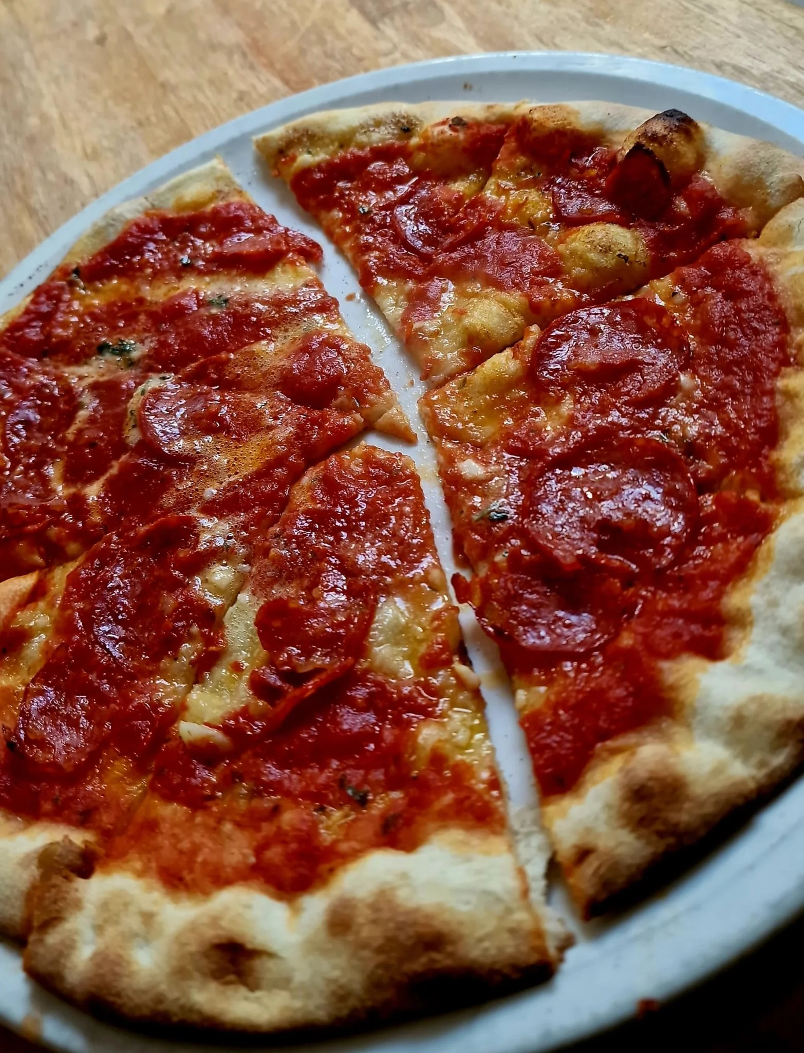 A pizza with pepperoni slices, cheese, and tomato sauce on a white plate.
