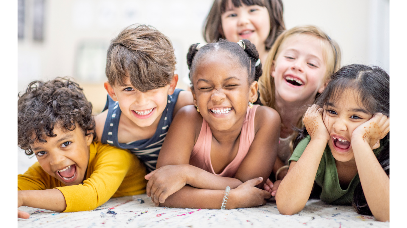 Six diverse and inclusive children lying on the floor, smiling and laughing together.