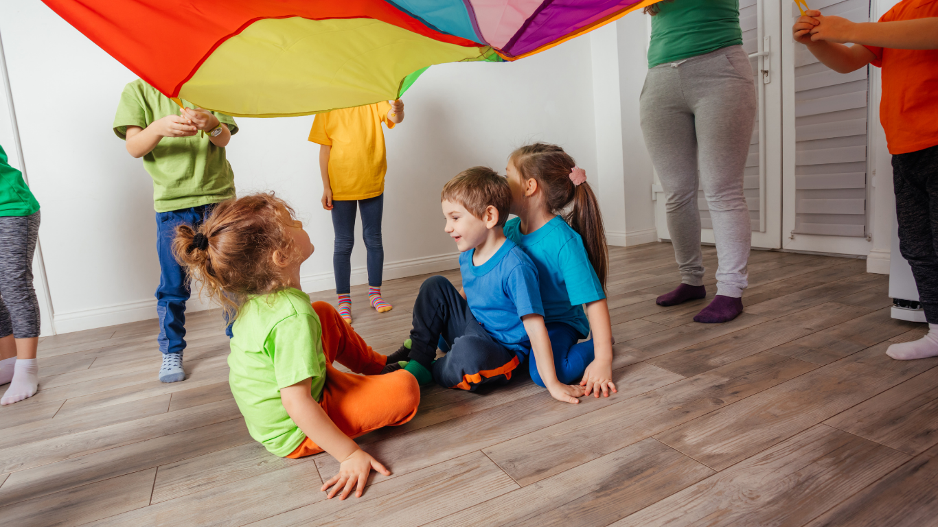 Children playing a movement game with a colorful parachute during a kids yoga and mindfulness class, building coordination and social skills.
