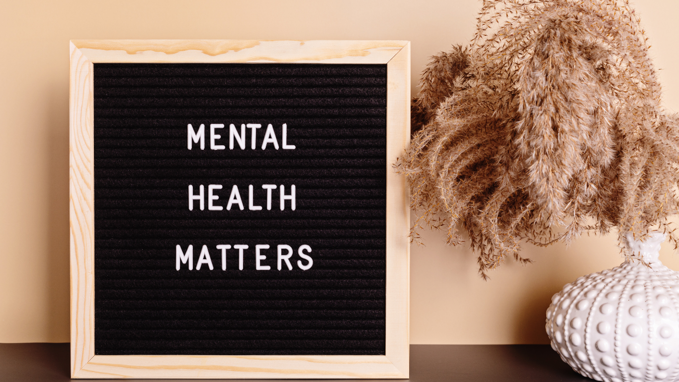 A framed black felt letter board displaying the words “Mental Health Matters,” styled on a neutral surface beside a white ceramic vase with dried pampas grass.