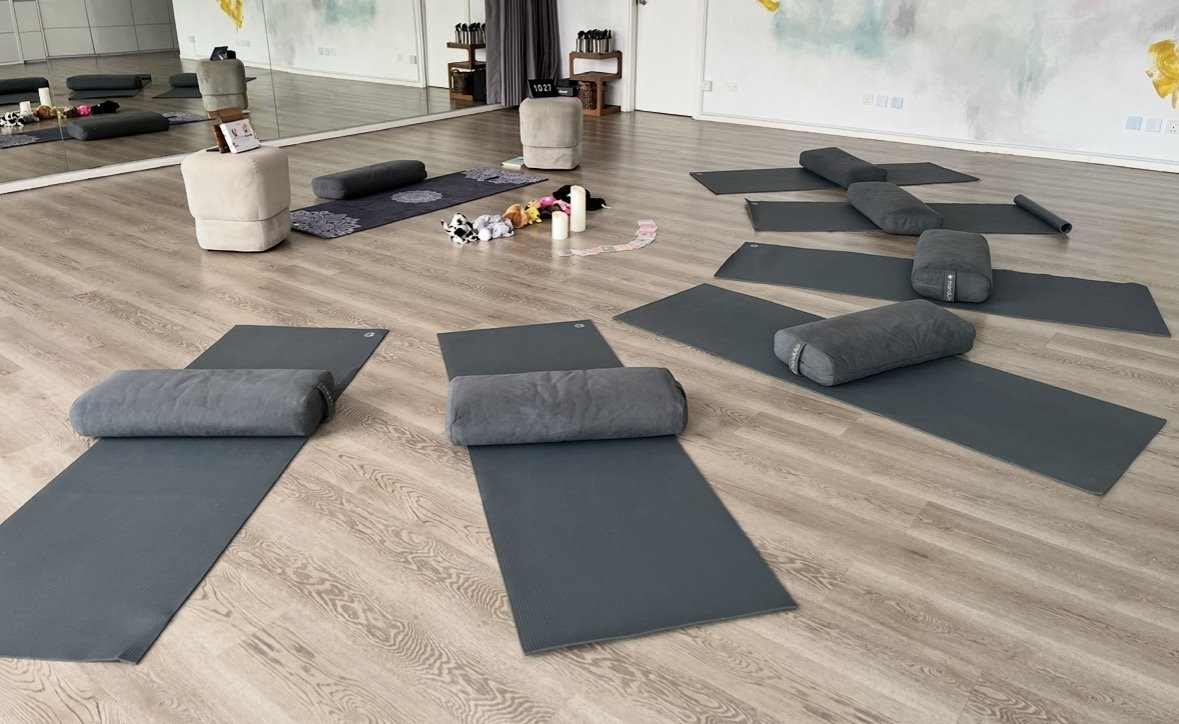 A bright yoga studio set up for children’s yoga classes, with yoga mats and bolsters evenly spaced on a wooden floor.