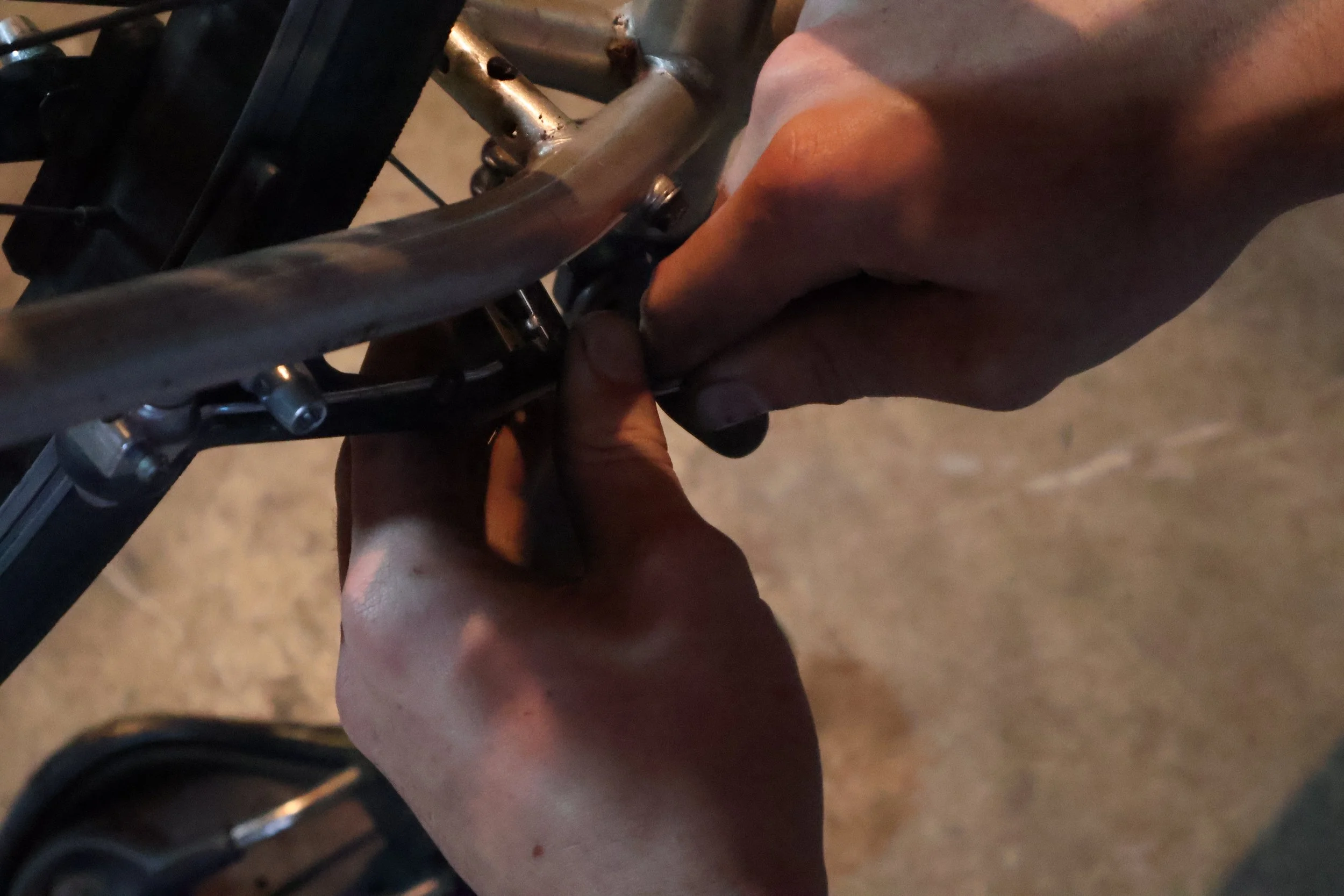 A person fixing or adjusting a handcycle, using their hands to work on the metal frame.