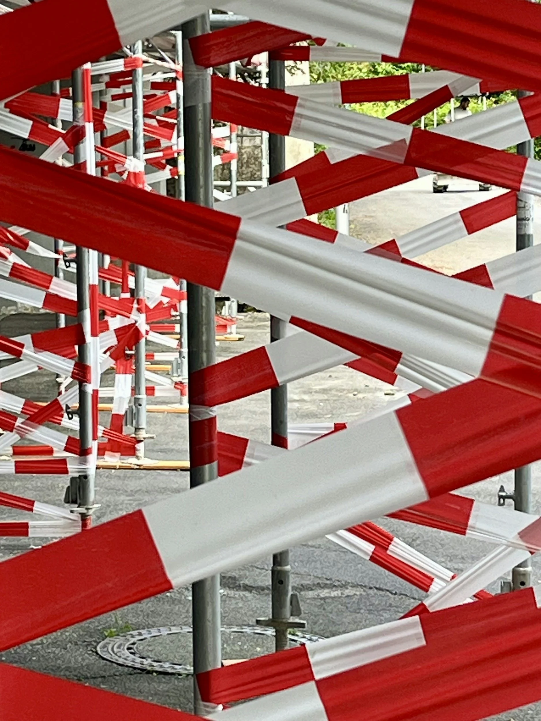 Scaffolding wrapped with red and white plastic safety tape, indicating a construction or restricted area.