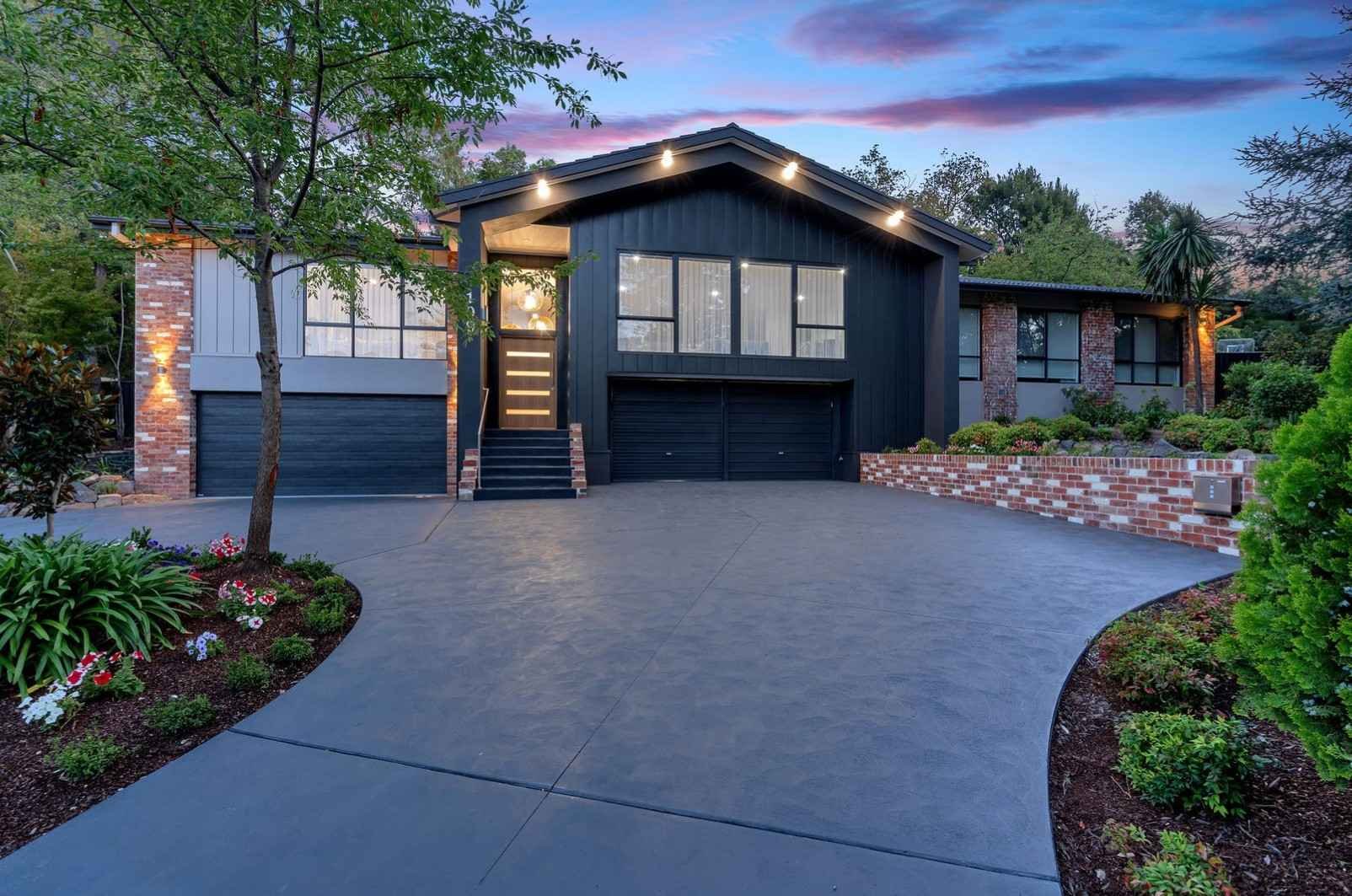 Modern house with large windows, brick accents, and a well-maintained front yard with lush green grass, shrubs, and trees, under a clear blue sky.