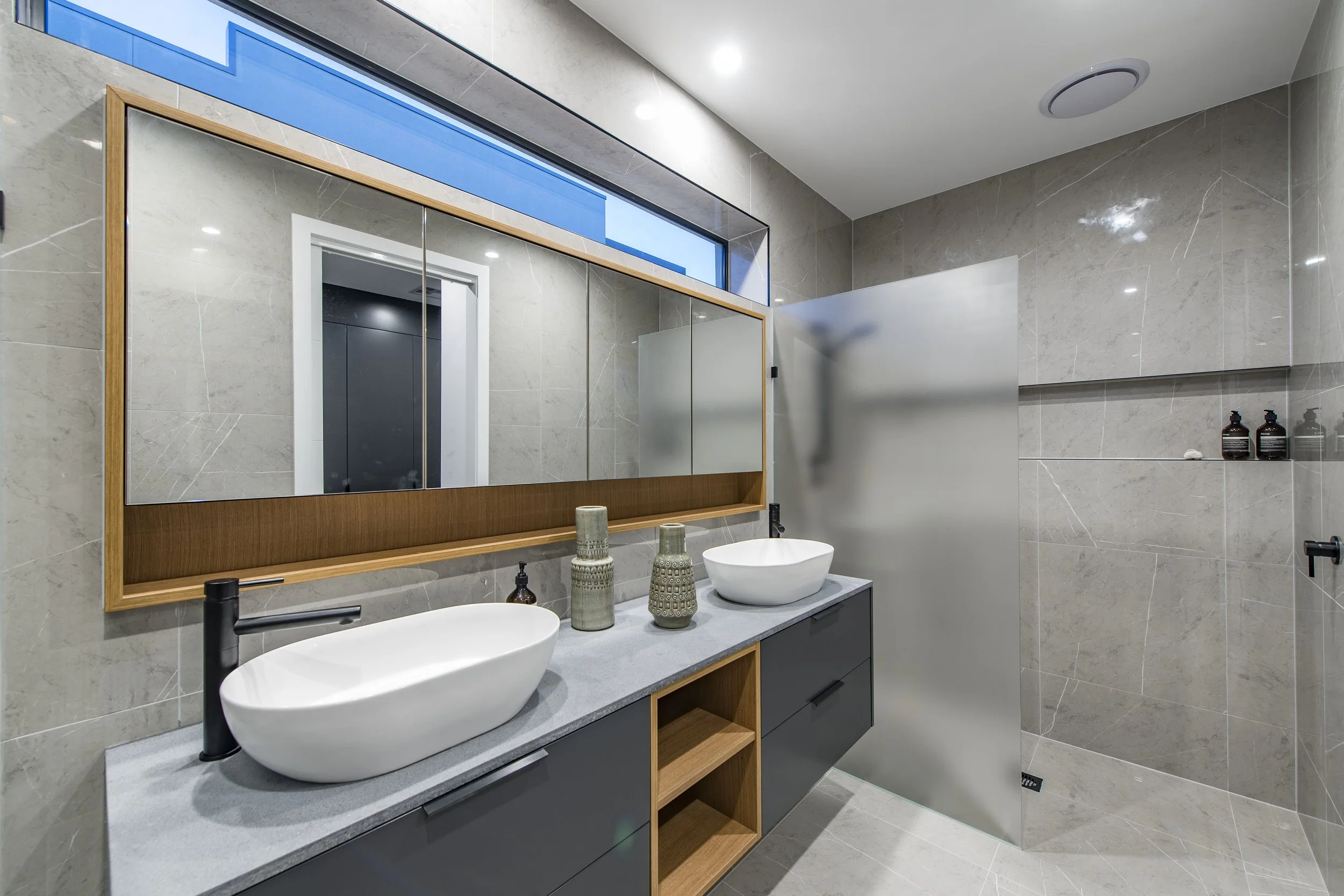 Modern bathroom with dual vessel sinks, large mirror, and beige marble walls and floors.
