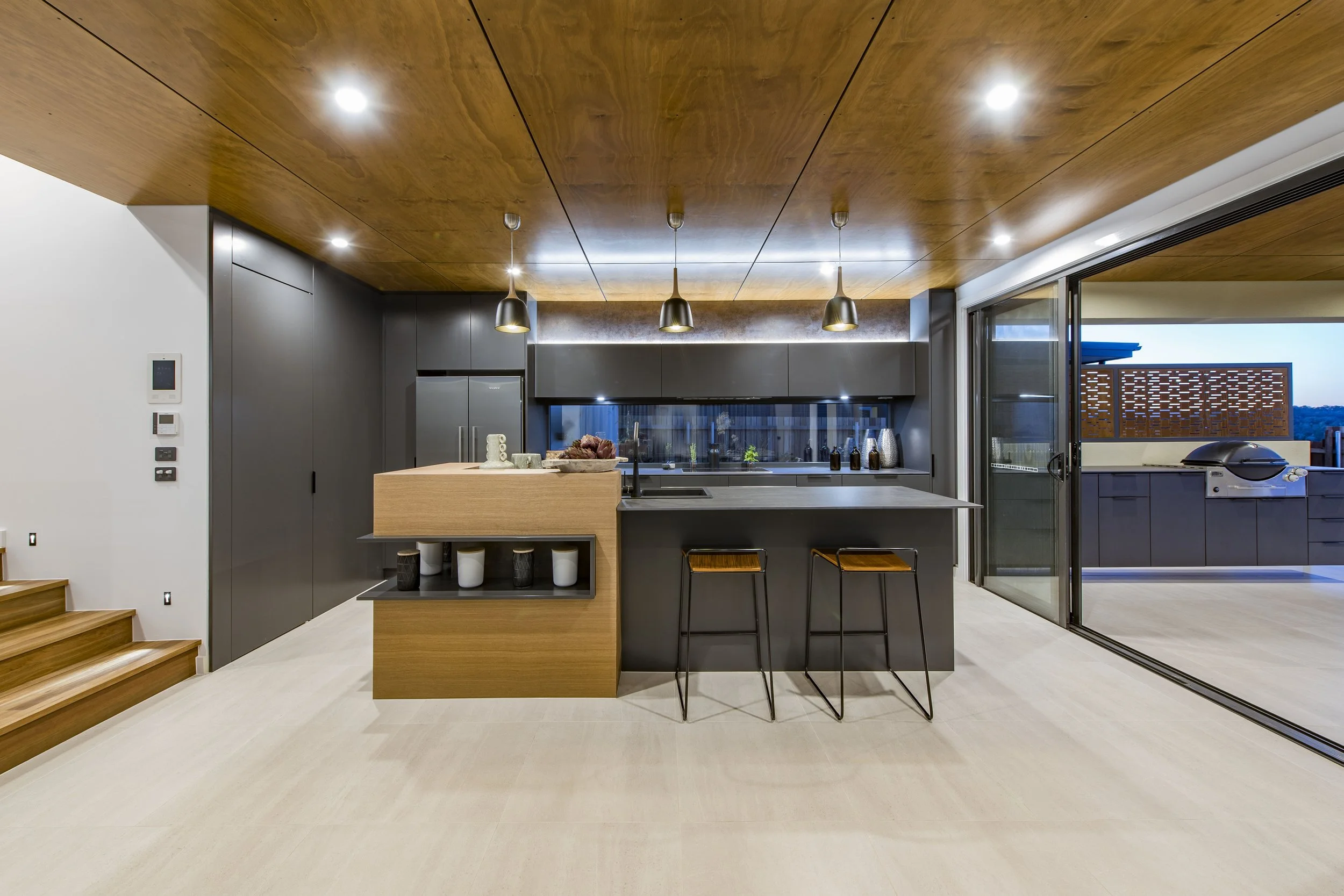 Modern kitchen with wooden ceiling, gray cabinets, black and wooden island, and sliding glass door leading to outdoor space.